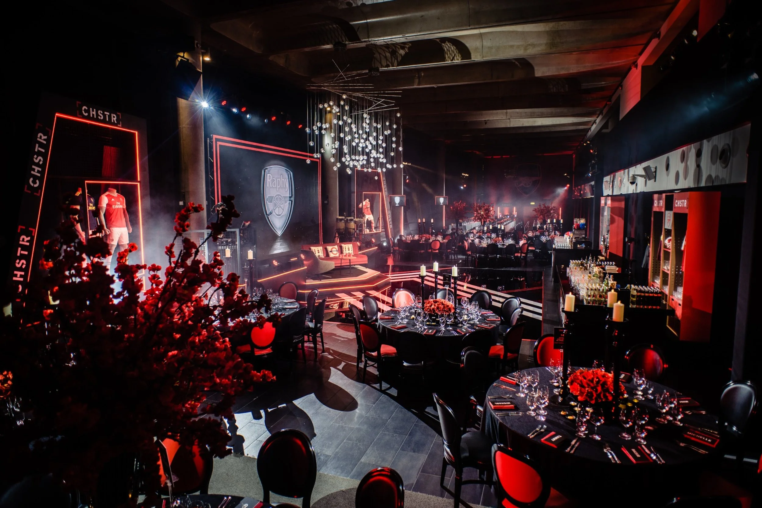 Emerates Stadium Bar Mitzvah sports celebration with Arsenal colours, red and black. The background features a stage with a large screen displaying a logo, mannequins wearing sports jerseys for a Match day energy