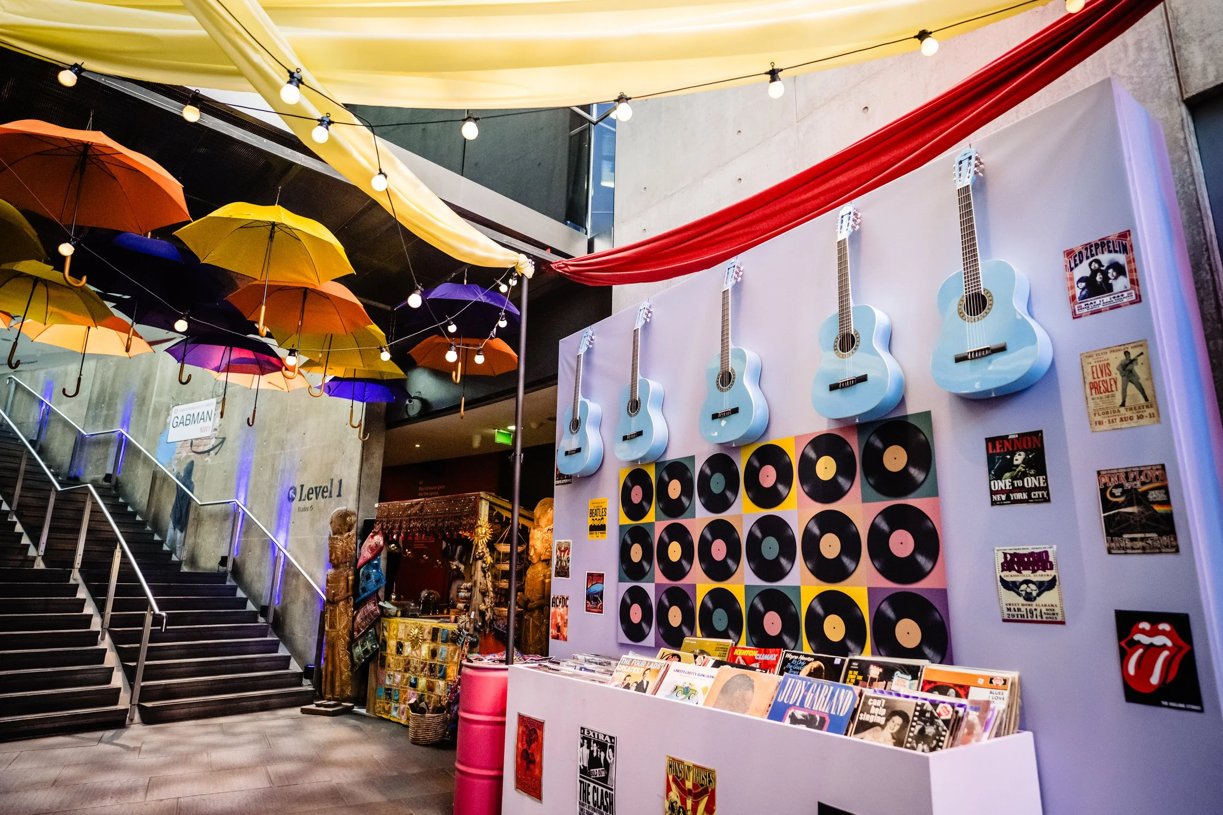 Interior of a music or pop culture store with hanging umbrellas, string lights, wall decorated with blue guitars and records, and a display of vinyl records and posters.
