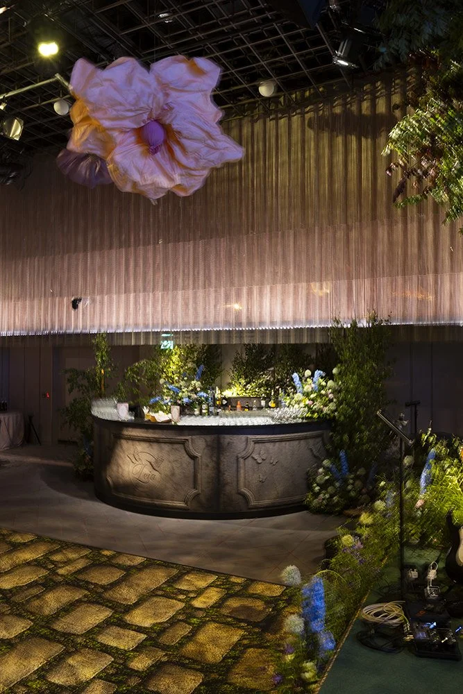 Garden bar at The Londoner for a Midsummer Night's Dream celebration, with a carved stone bar, oversized flower sculpture overhead and cobbled flooring