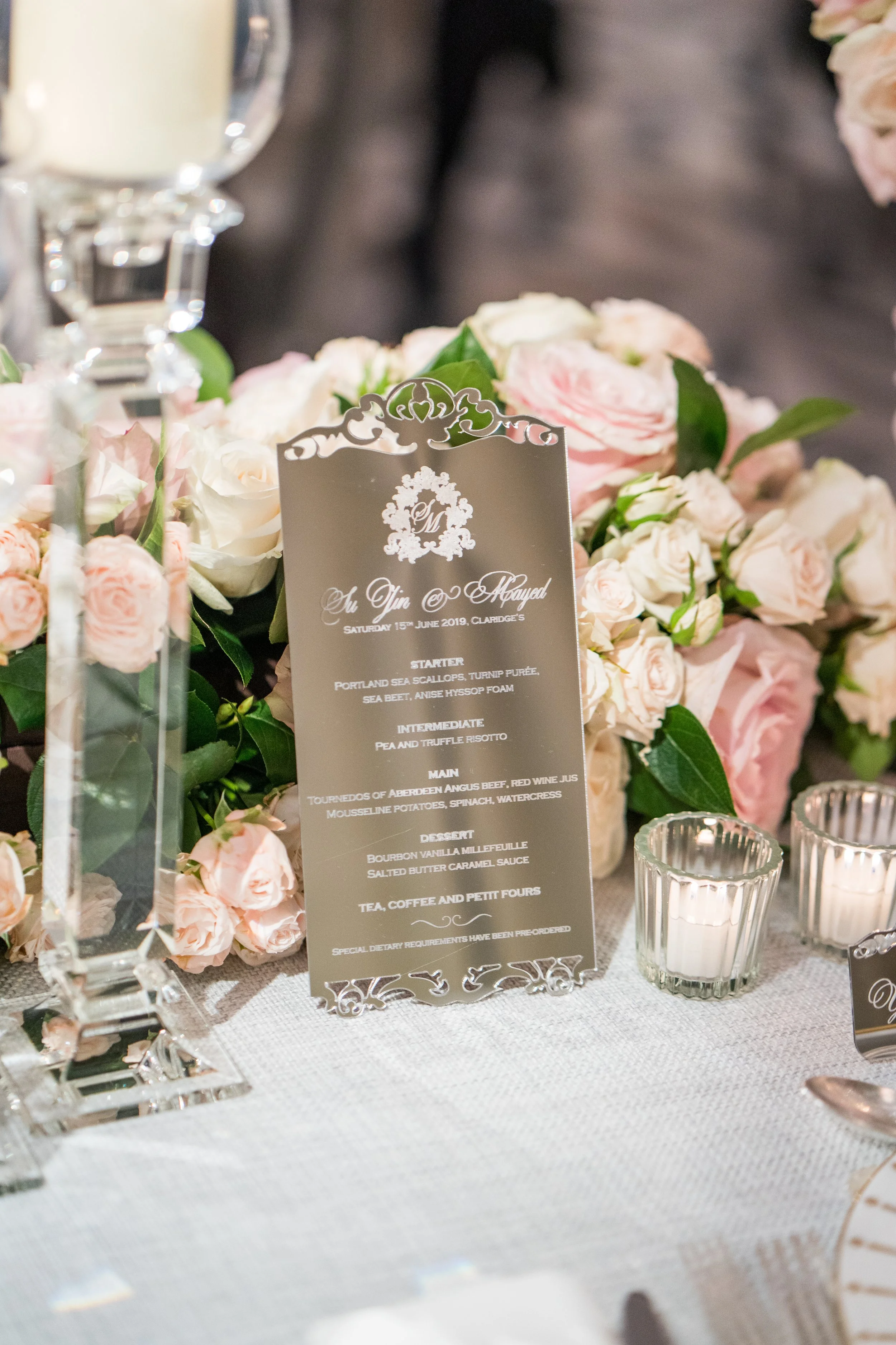 A wedding reception table with a floral centerpiece, a decorative menu card, and candle holders.