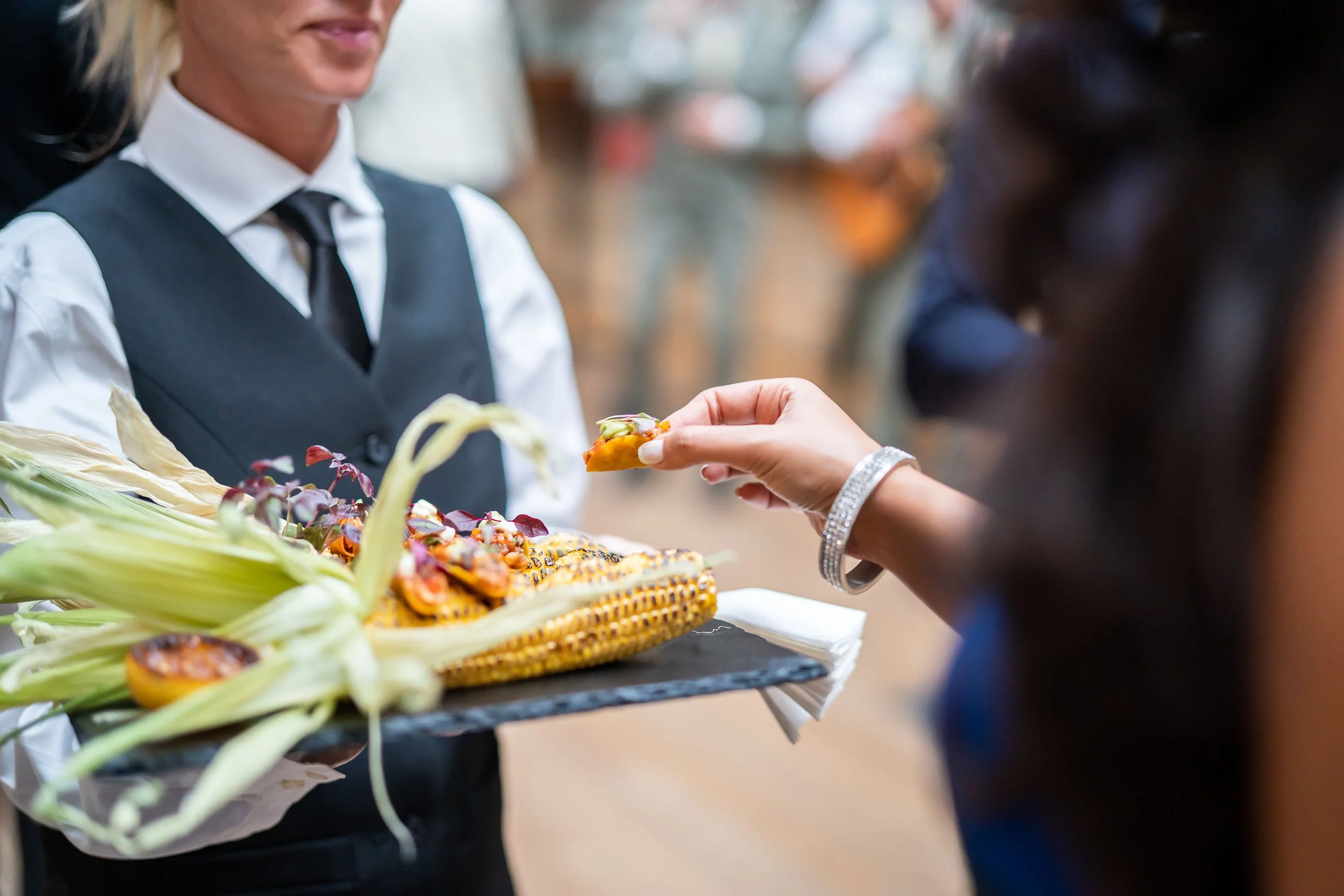 A server dressed in a white shirt, black vest, and black tie handing a piece of food to a customer at The Natural History Museum
