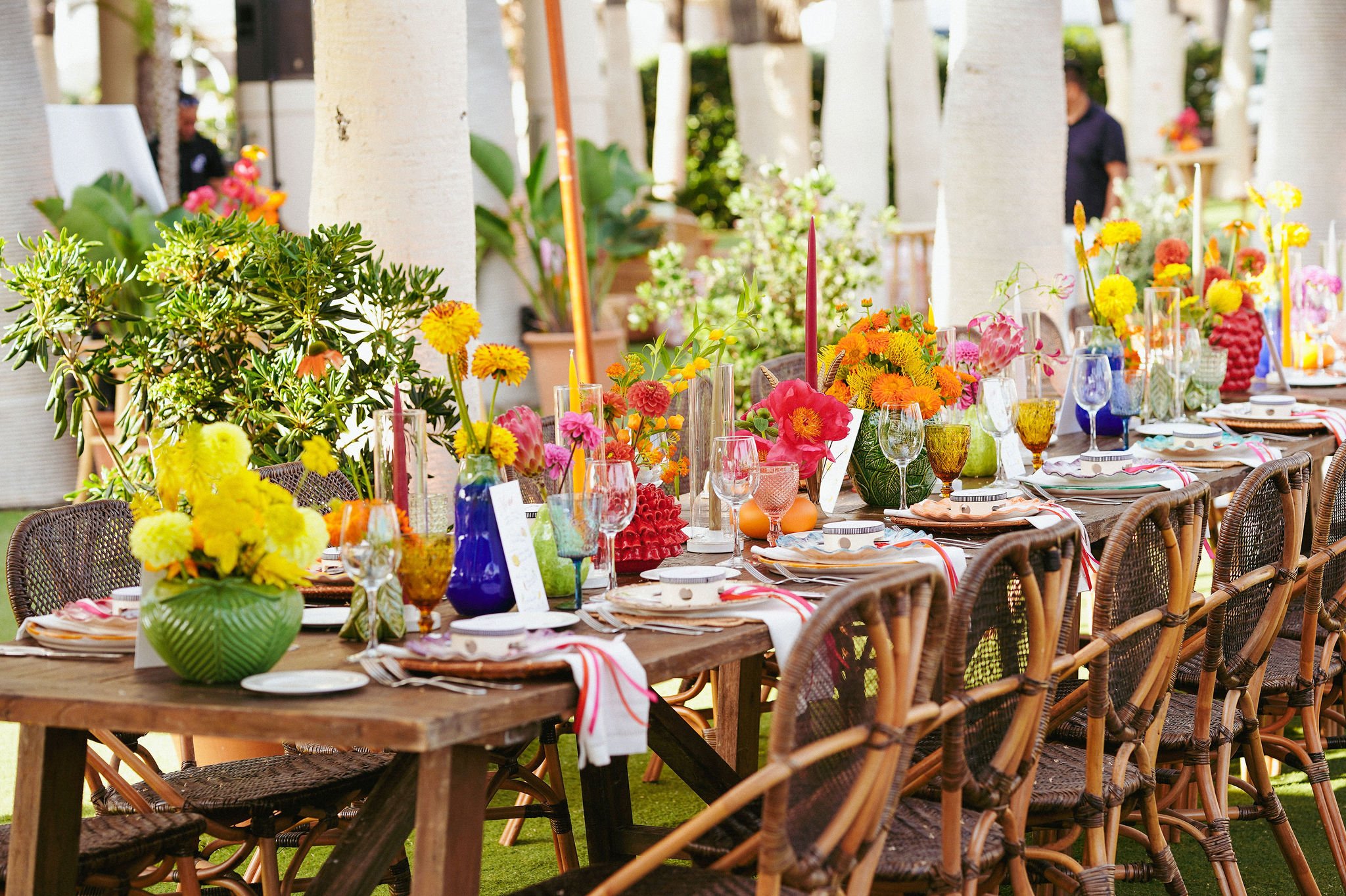 A long wooden table set up outdoors with colorful floral centerpieces, glassware, plates, and cutlery for a celebration or event, with greenery and trees in the background at Anantara Villa Padierna Resort in Marbella
