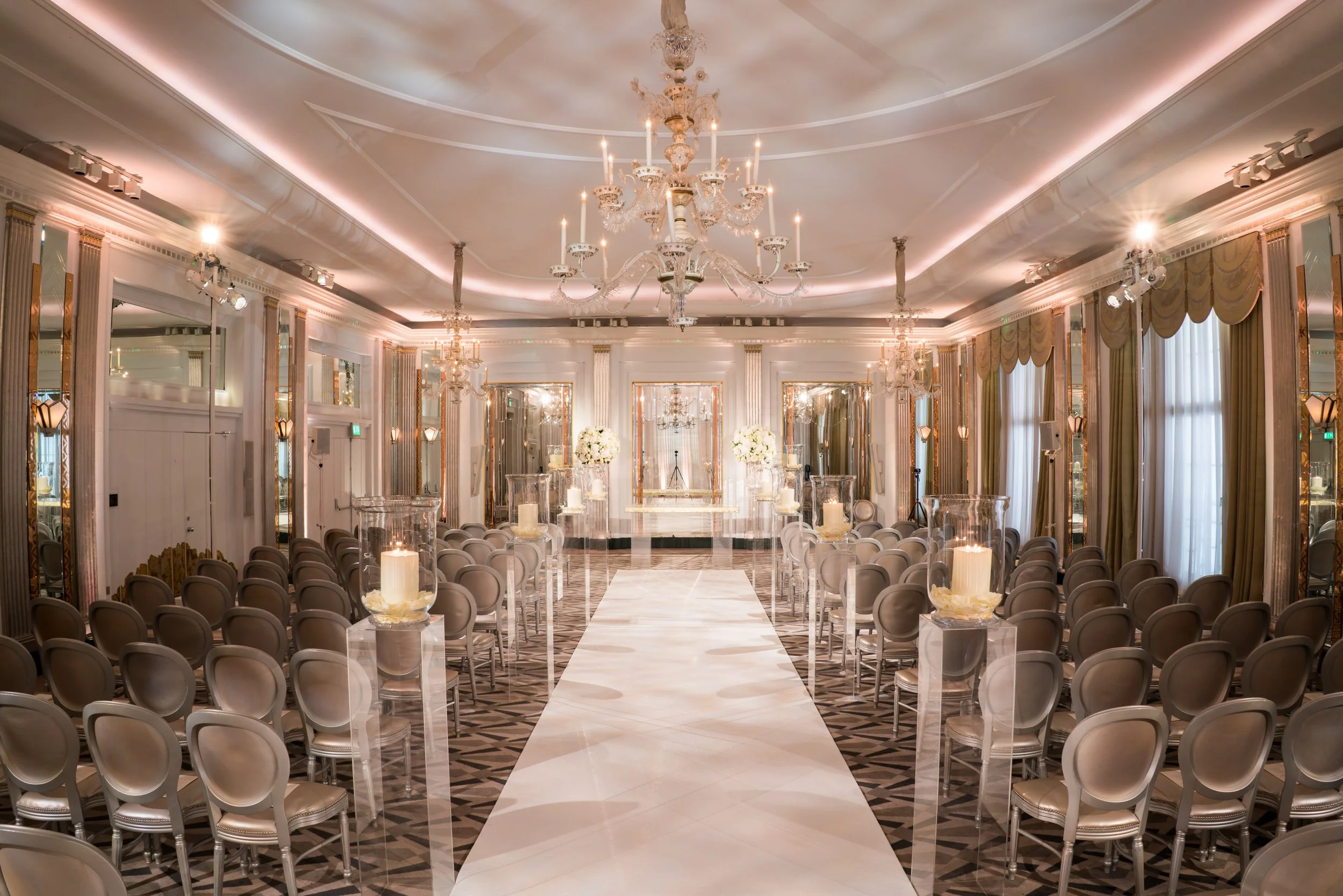 An elegant event hall decorated with chandeliers, large mirrors, candles, and drapes, prepared for a wedding or formal gathering.