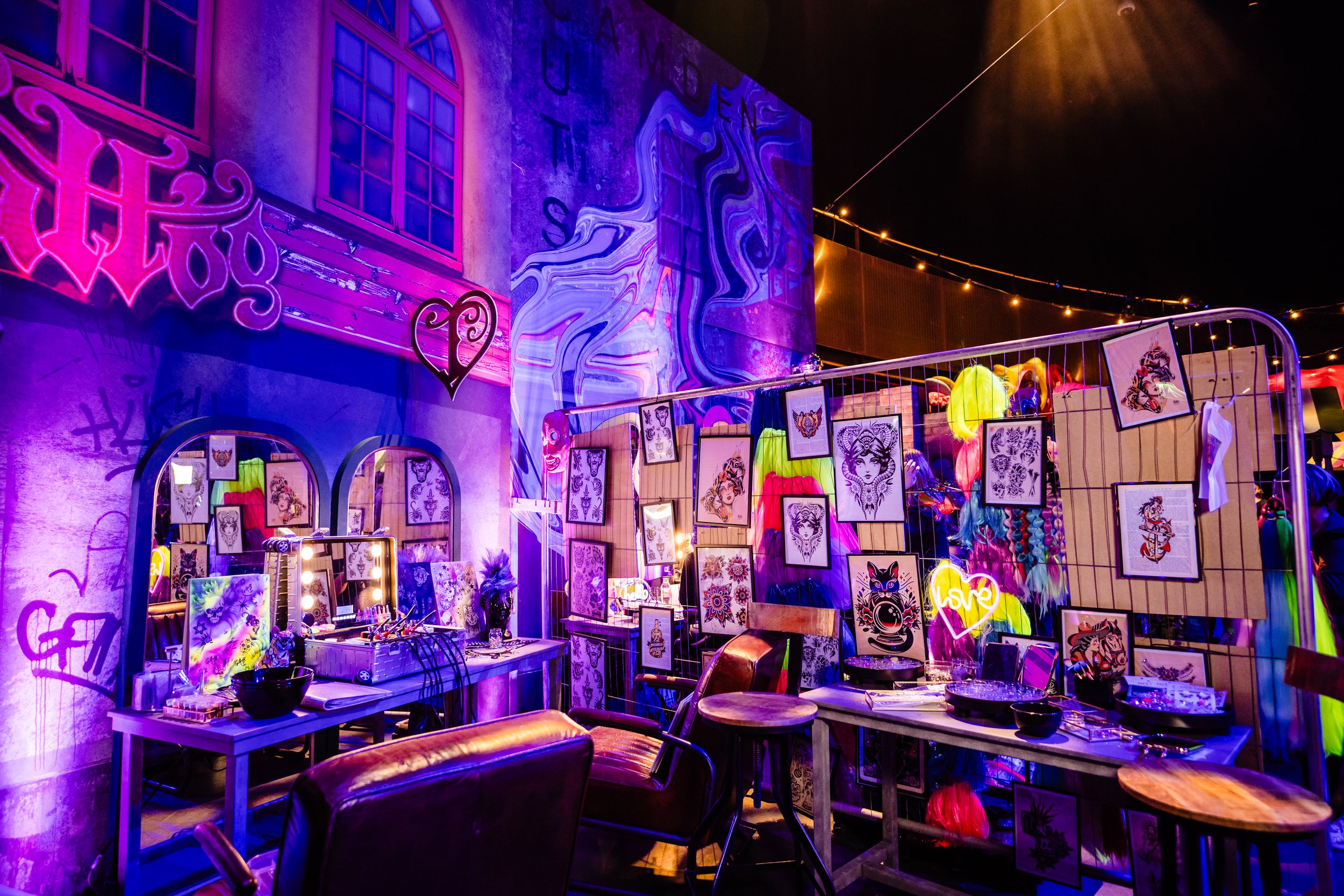 Tattoo art display at an indoor Bar Mitzvah , featuring neon and LED lighting, with framed artwork and tattoos on display, decorative string lights, and colorful balloons in the background.