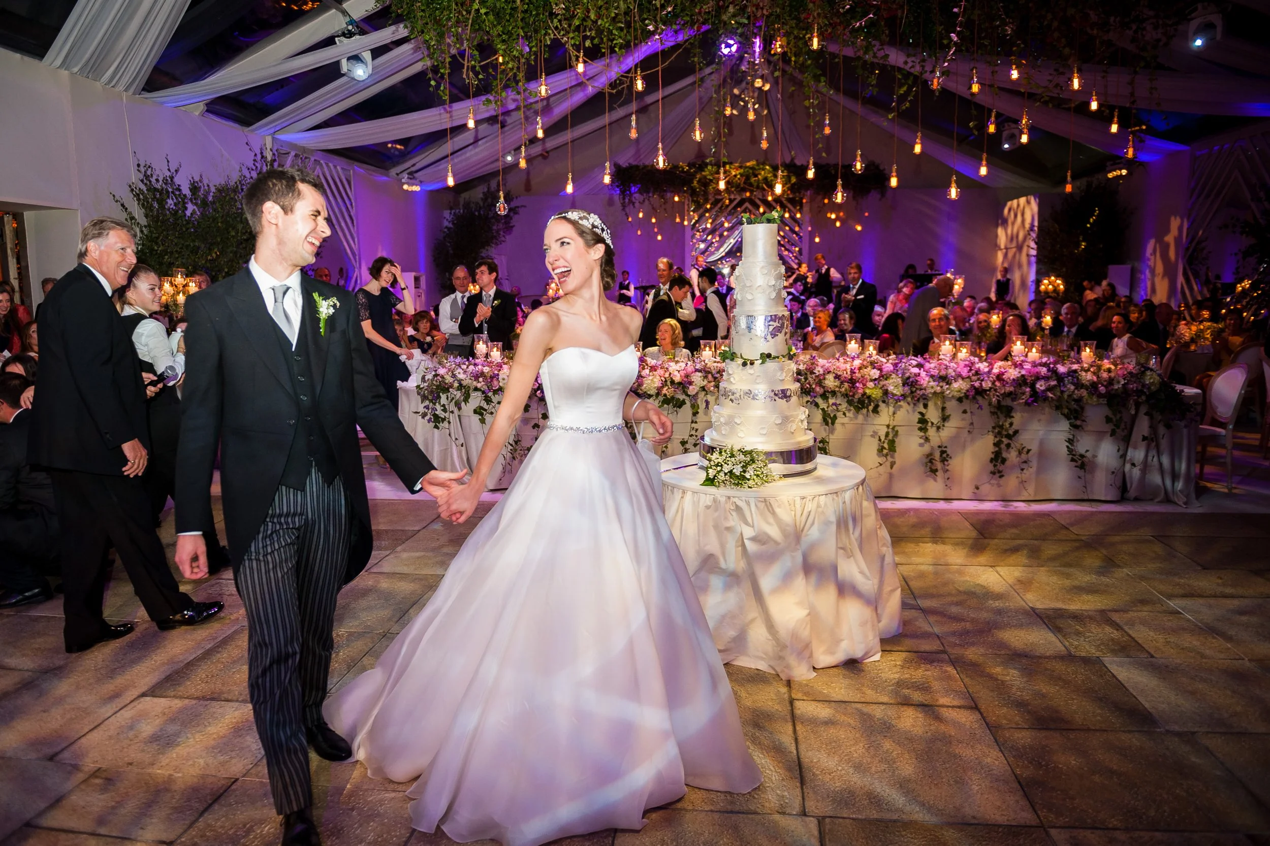 Bride and groom dancing at wedding reception with guests and floral decor in the background.