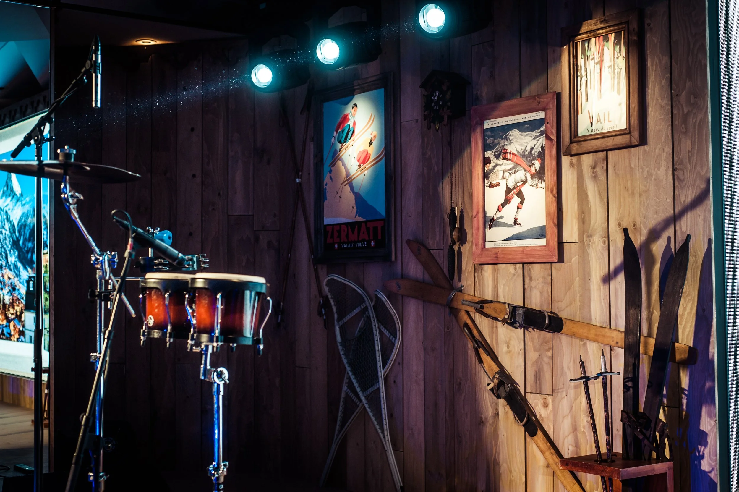 A corner of a room decorated with vintage ski posters, skis, and musical instruments, illuminated by blue lighting.