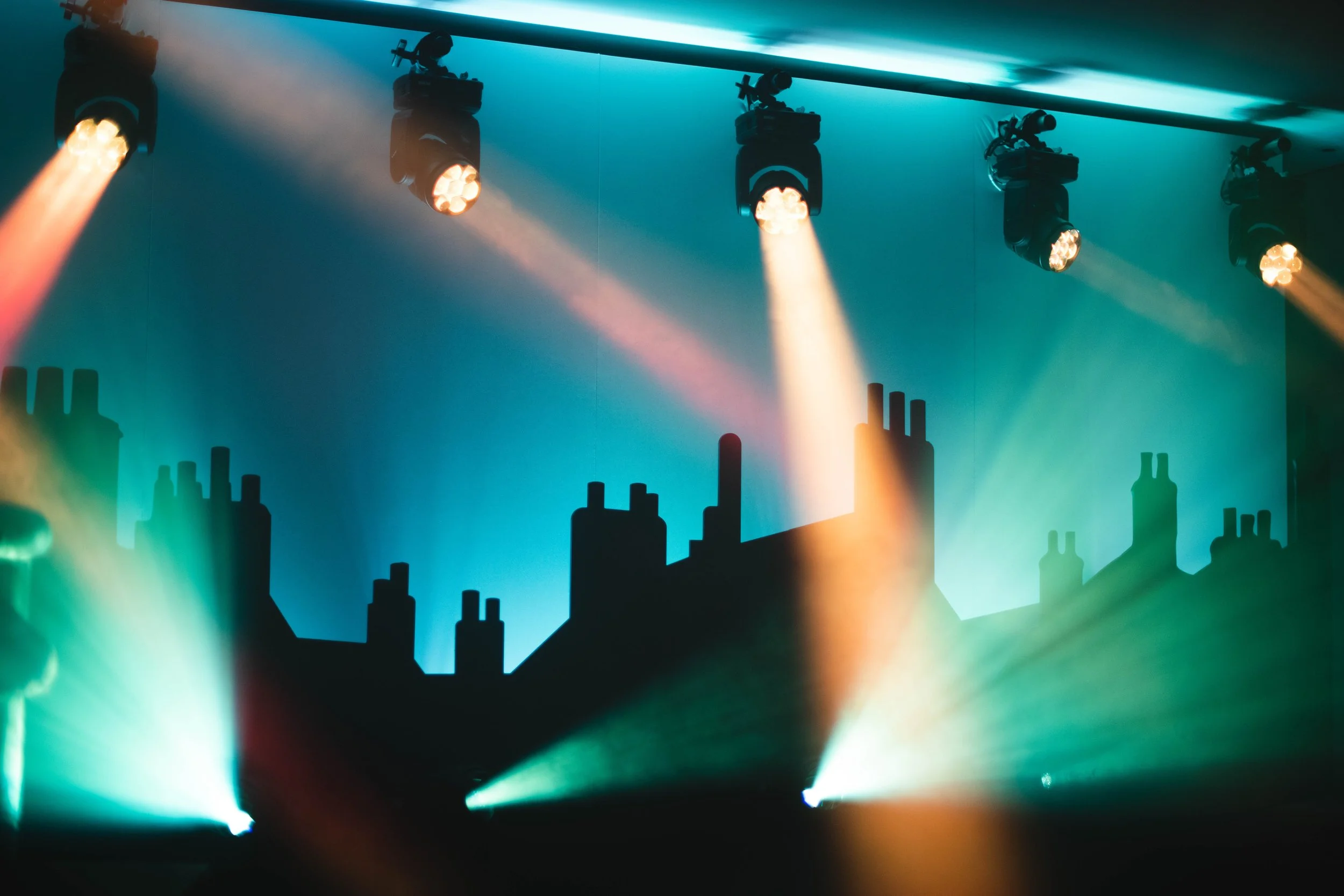 Stage lighting with colorful spotlights and silhouettes of industrial chimney shapes projected on the wall.