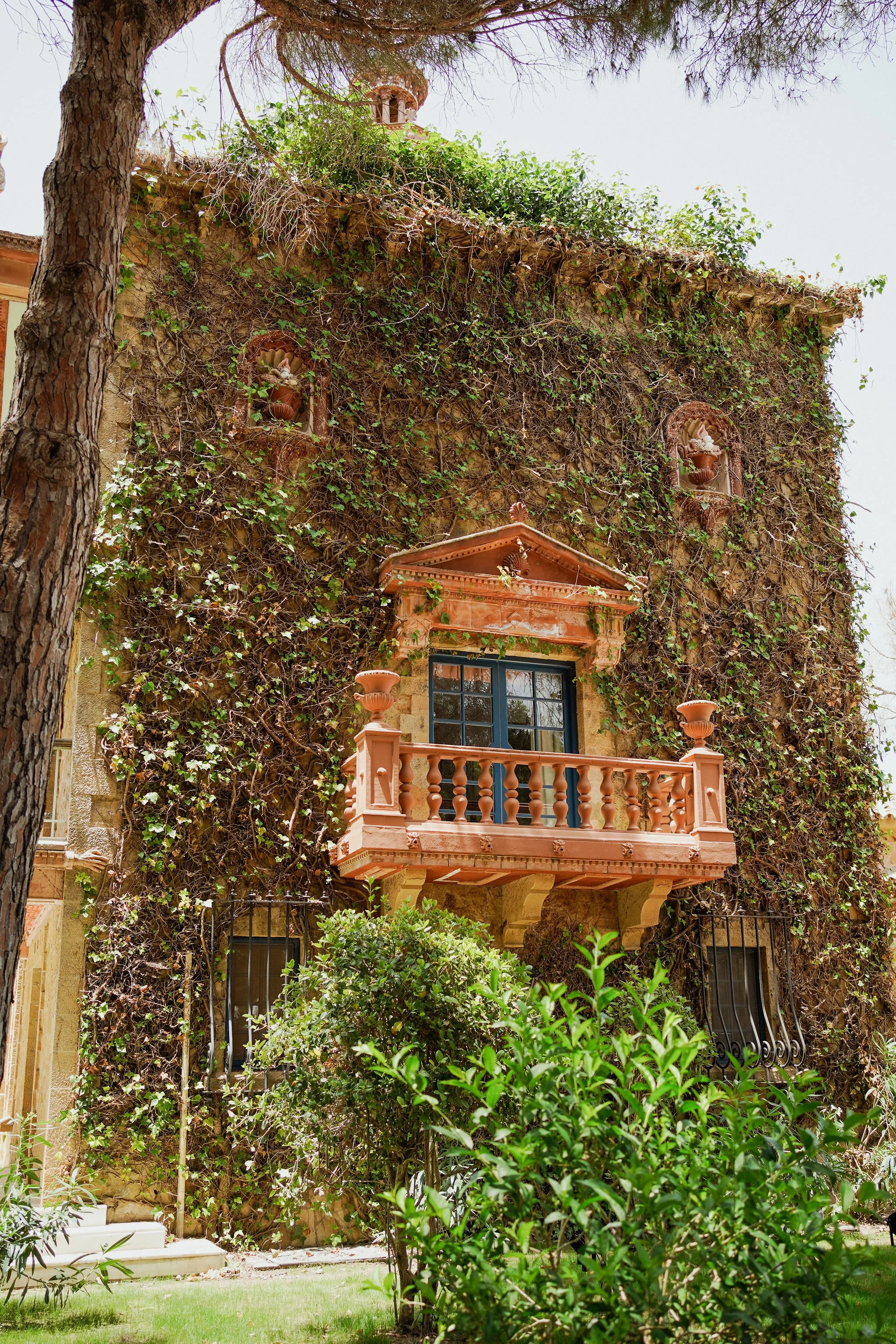 A building with a pink balcony and window, covered in green vines and ivy, surrounded by bushes and trees at Anantara Villa Padierna Resort in Marbella