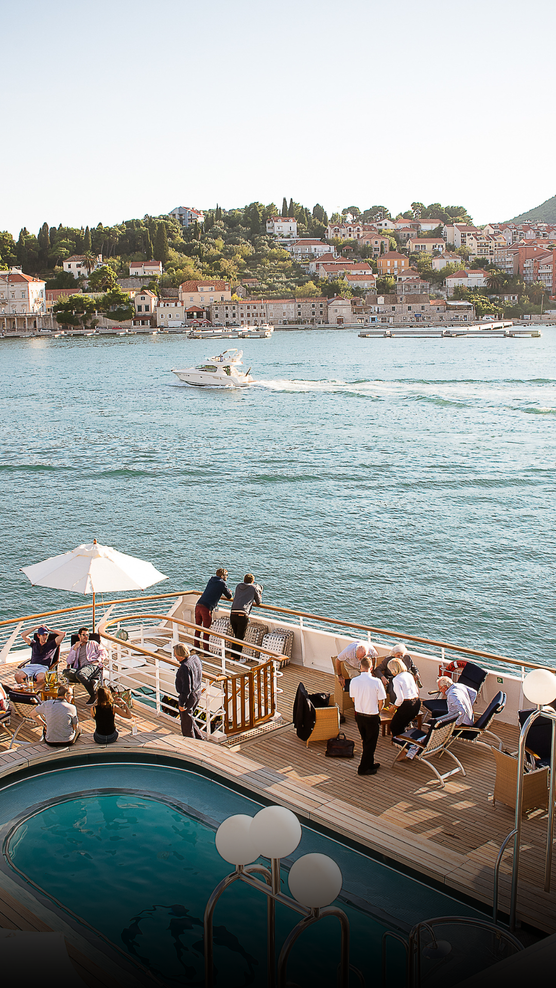 Brand experience event on a yacht where people are relaxing and socializing on the deck of a boat or cruise ship, with a scenic coastal town and hillside homes visible in the background.