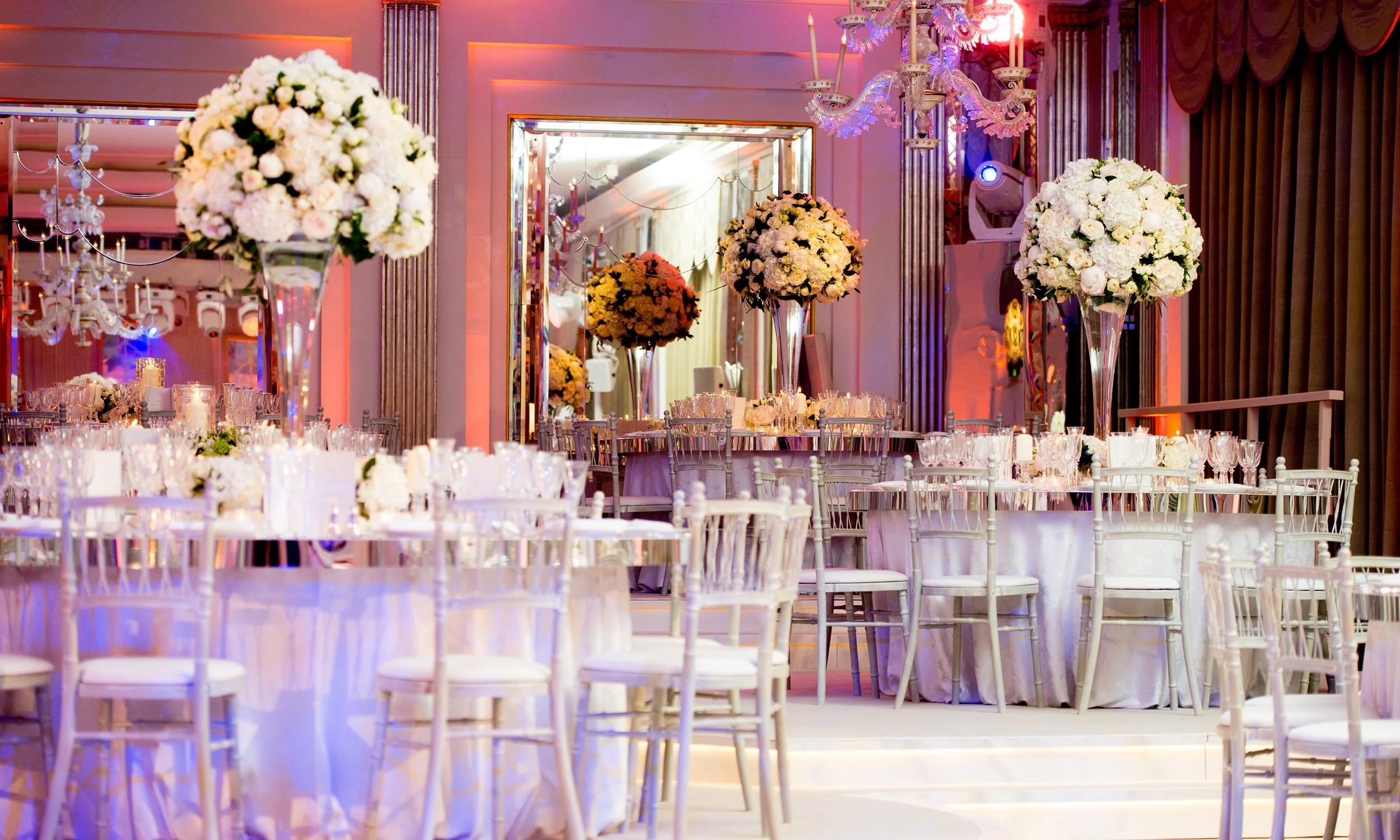 Elegant banquet hall decorated for a wedding with large floral centerpieces, chandeliers, and seating arrangements.