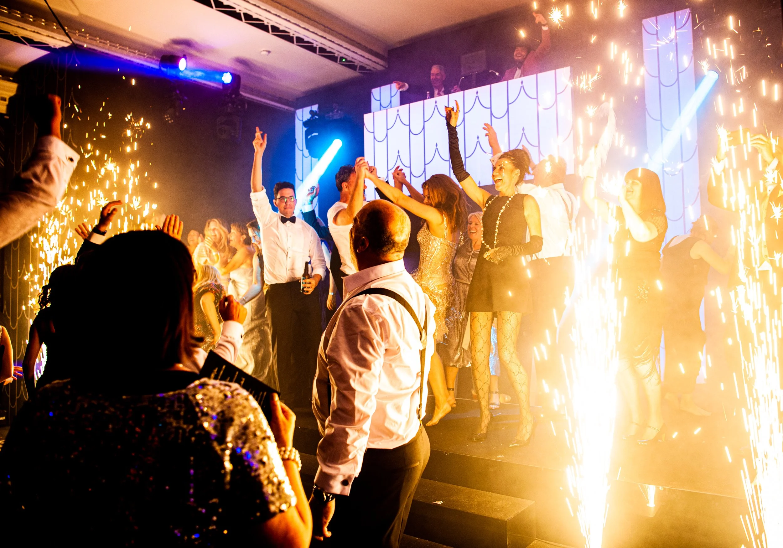 People dancing and celebrating on a dance floor with sparklers and bright lights at Claridge's decorated in a 50's themed party 
