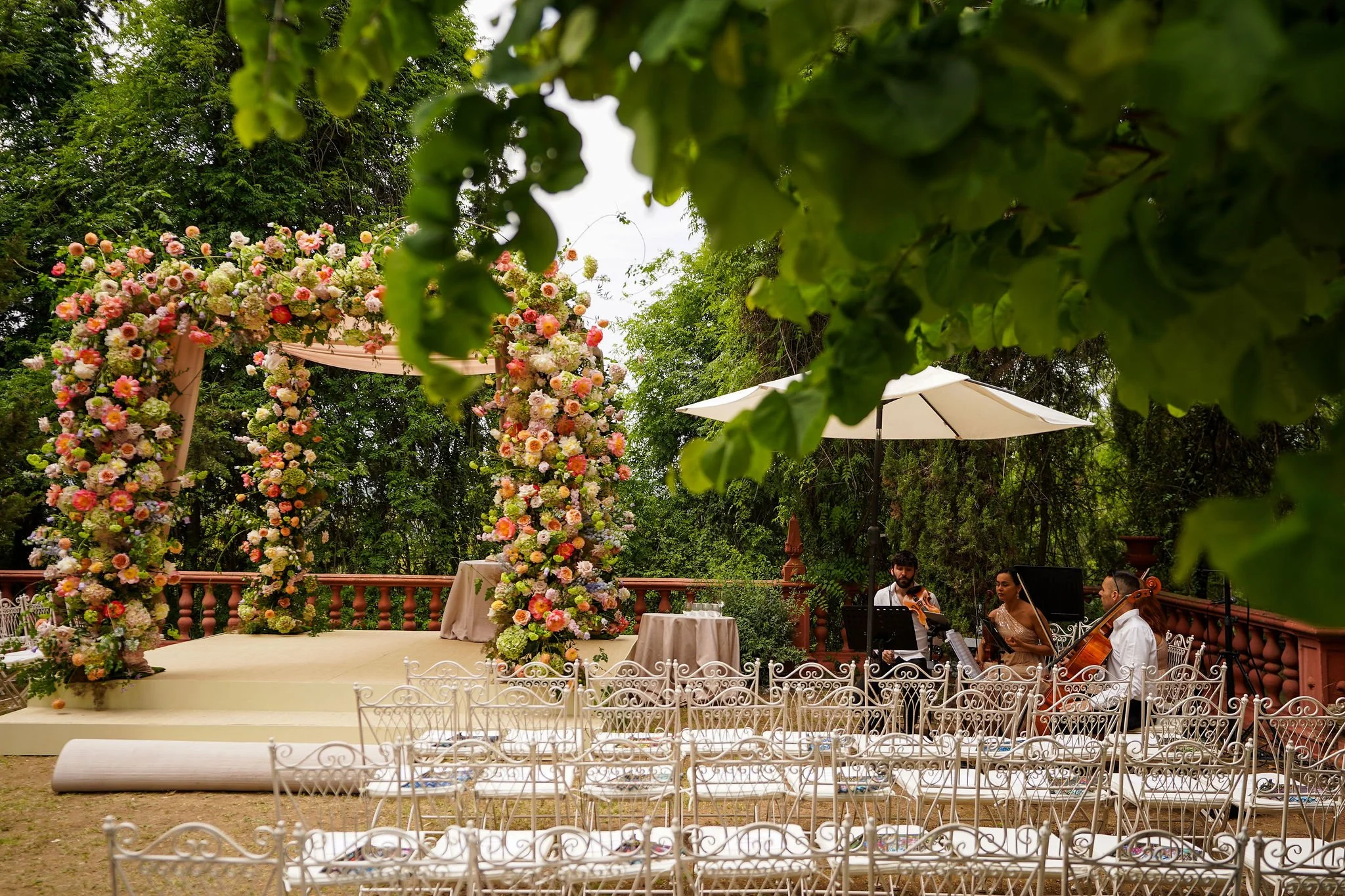 Elegant outdoor wedding ceremony setup with floral chuppah, white chairs, and musicians playing string instruments under trees and umbrellas at Anantara Villa Padierna Resort in Marbella