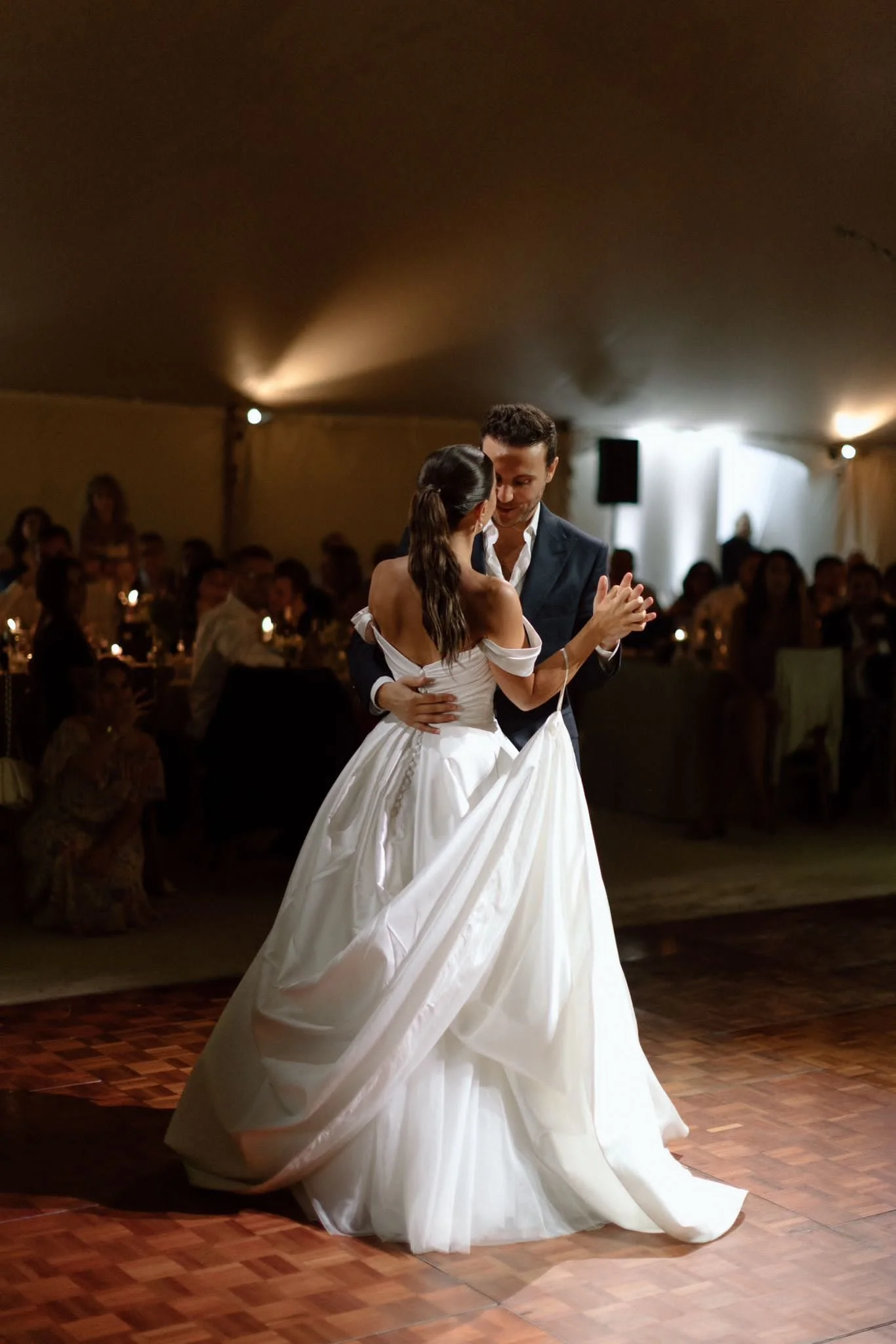 Couple dancing during their wedding reception, surrounded by guests in a decorated venue.