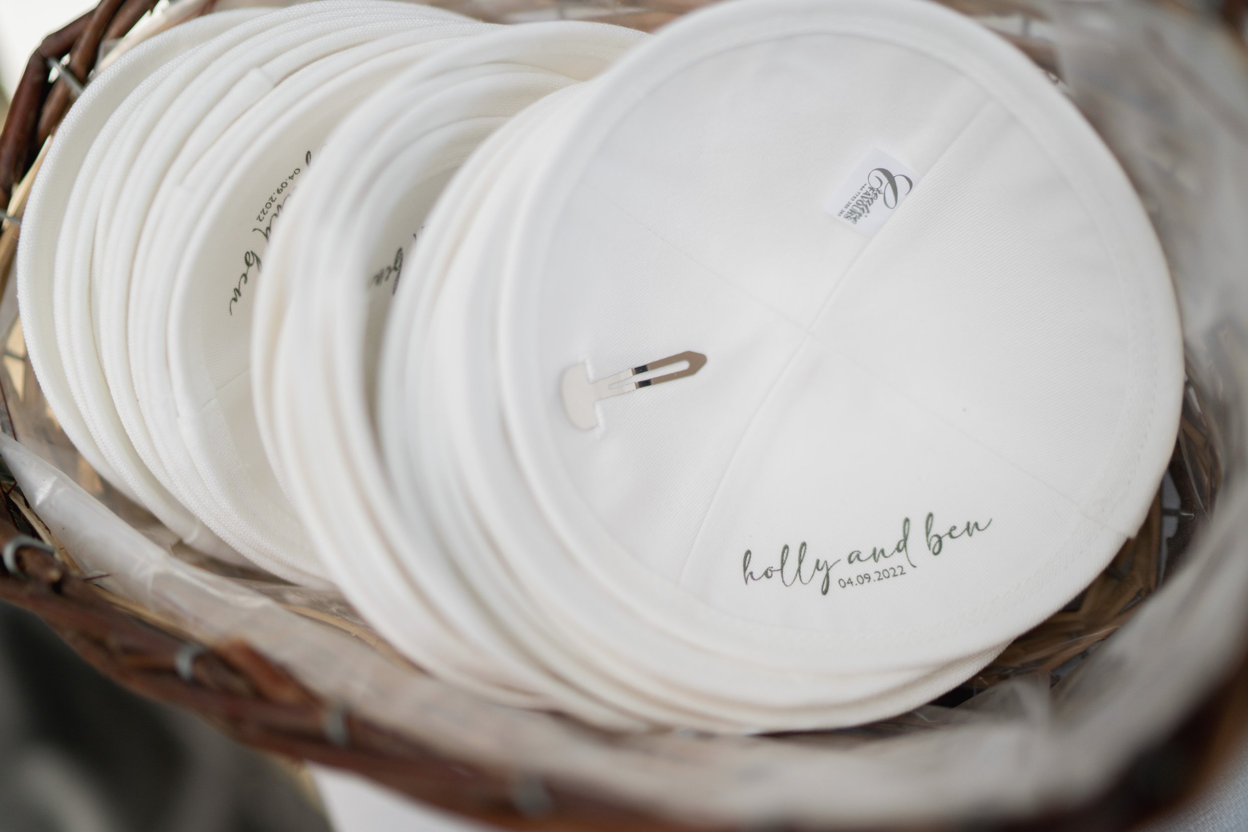A basket filled with white embroidered kippah with personalized text and date, for a private luxury wedding