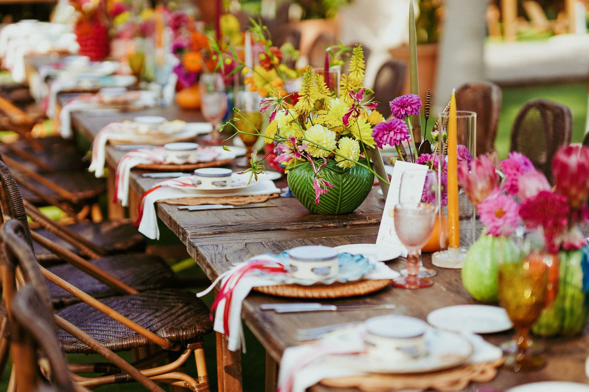 A long dining table set outdoors with floral centerpieces, candles, and place settings for the welcome dinner of wedding celebration at Anantara Villa Padierna Resort in Marbella