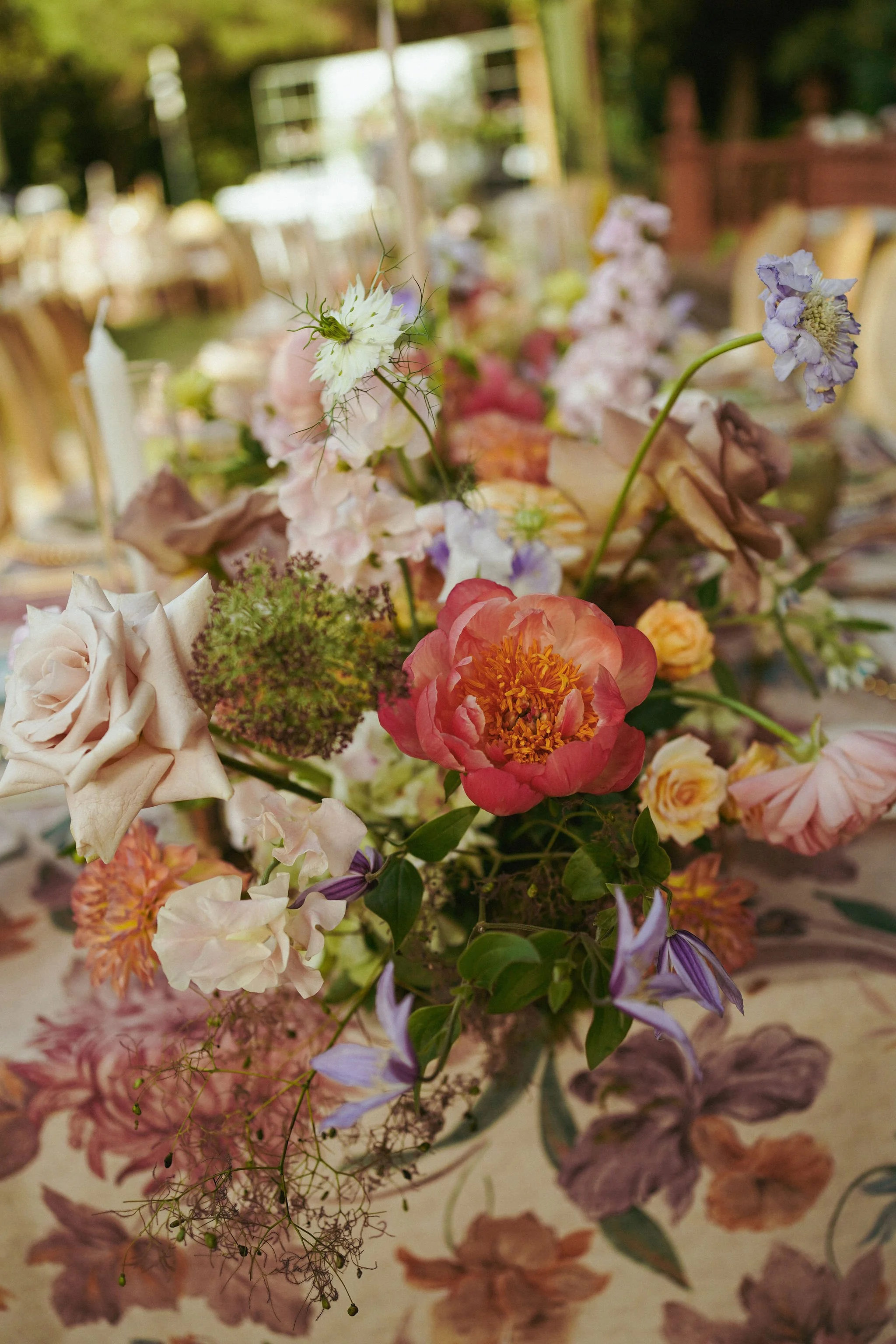 A floral arrangement with various colorful flowers, including pink, purple, white, and peach, and green foliage, placed on a table or surface.