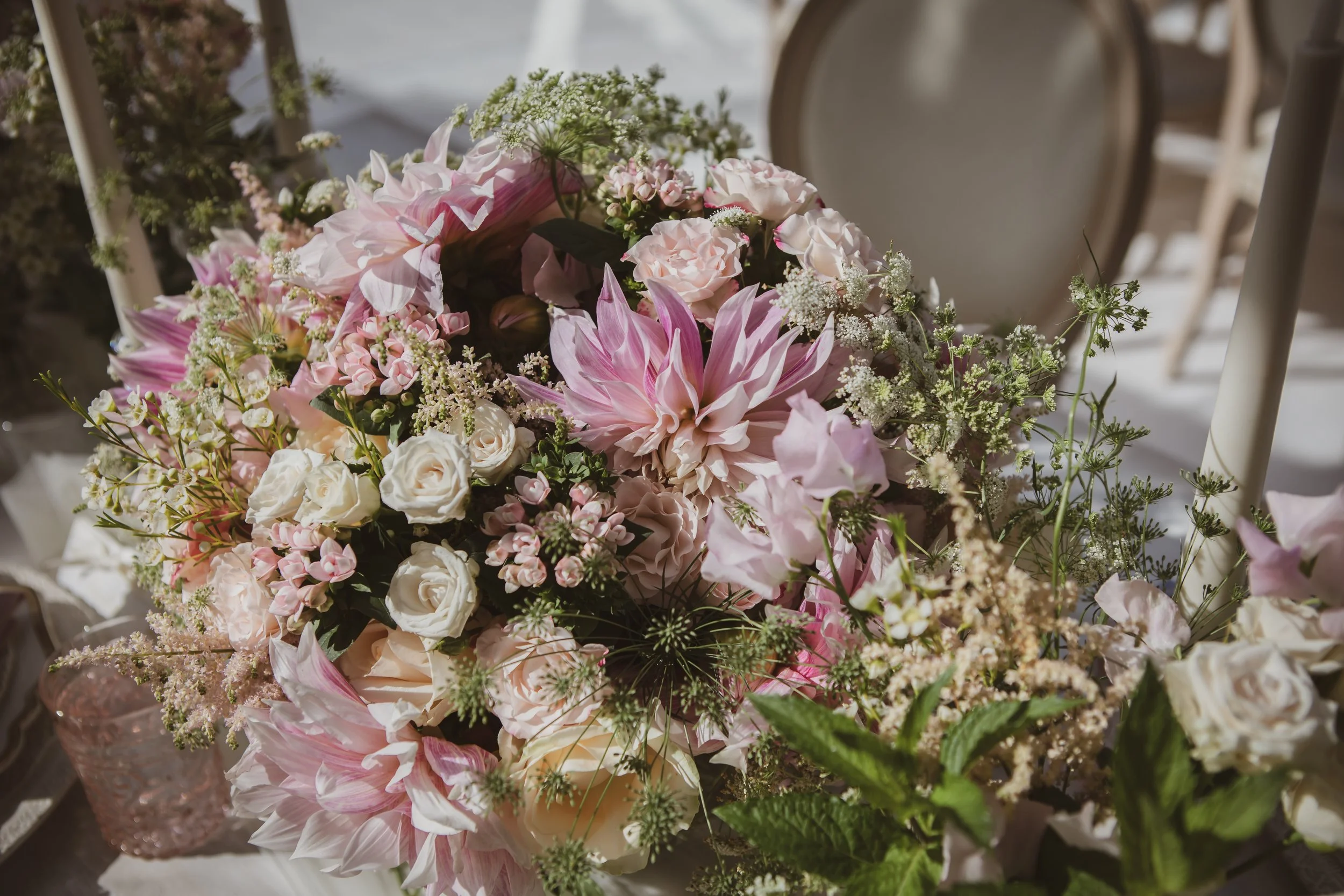 A bouquet of pink and white flowers, including roses and lilies, arranged in a glass vase with greenery and delicate white fillers.