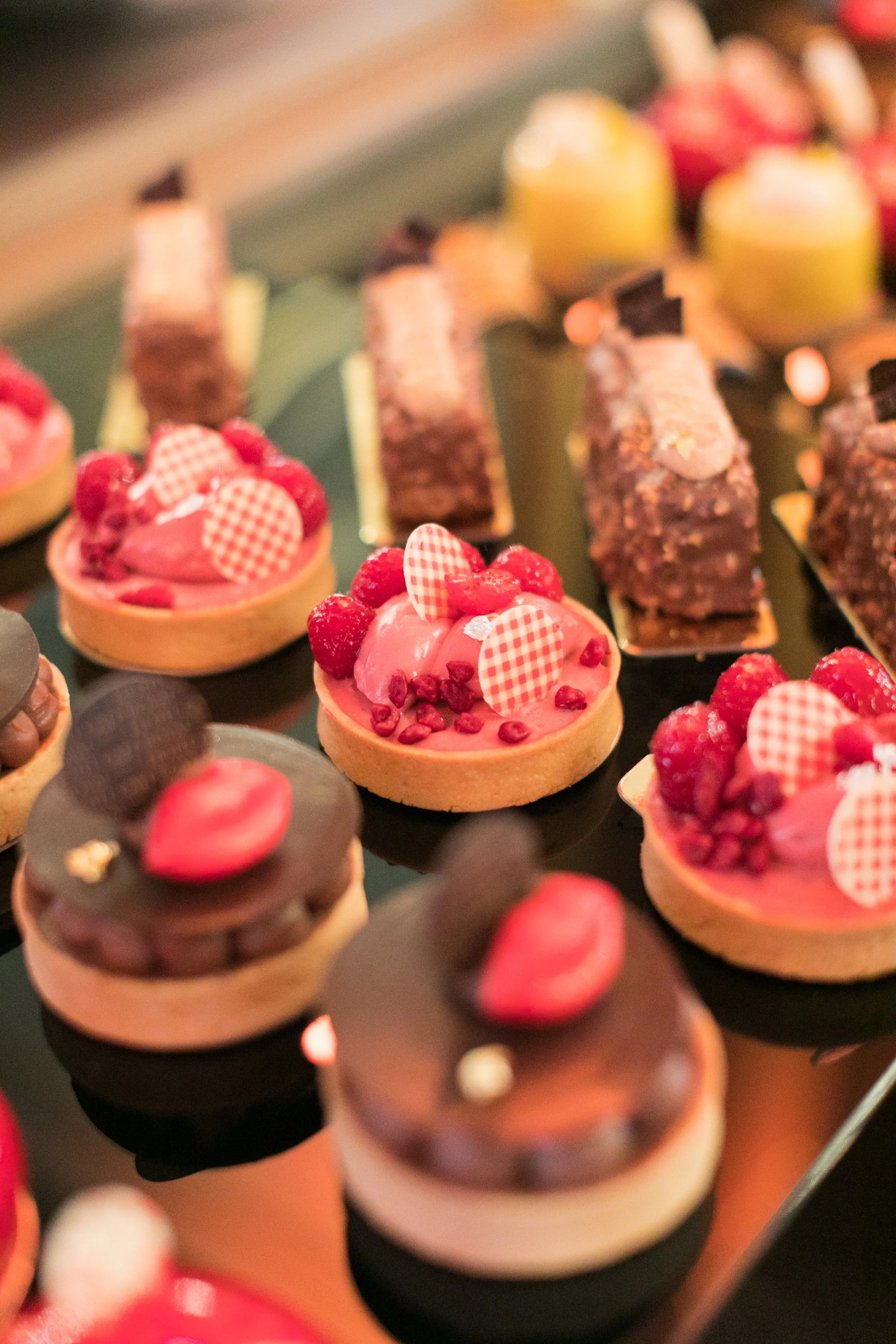 Assorted small pastries including fruit tarts with strawberries and raspberries, and chocolate-topped desserts, arranged on a tray.