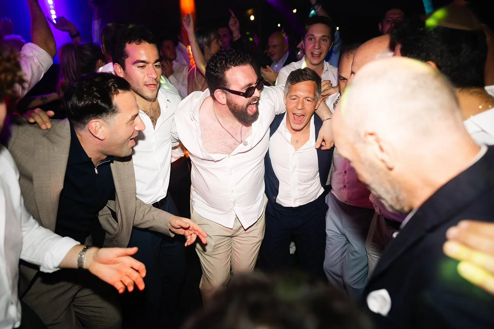 Group of men dancing and celebrating at the afterparty, smiling and with arms around each other.
