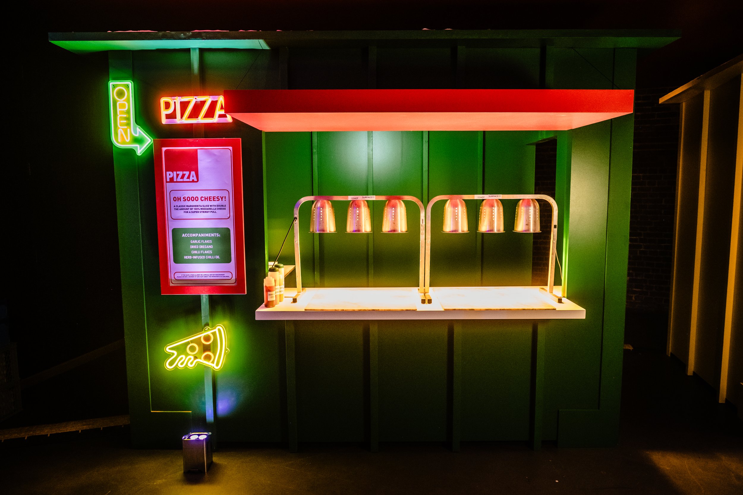Neon signage for a pizza stand, including bright green 'Open' sign, red 'Pizza' sign, and a cartoon neon pizza slice at a Bar Mitzvah 