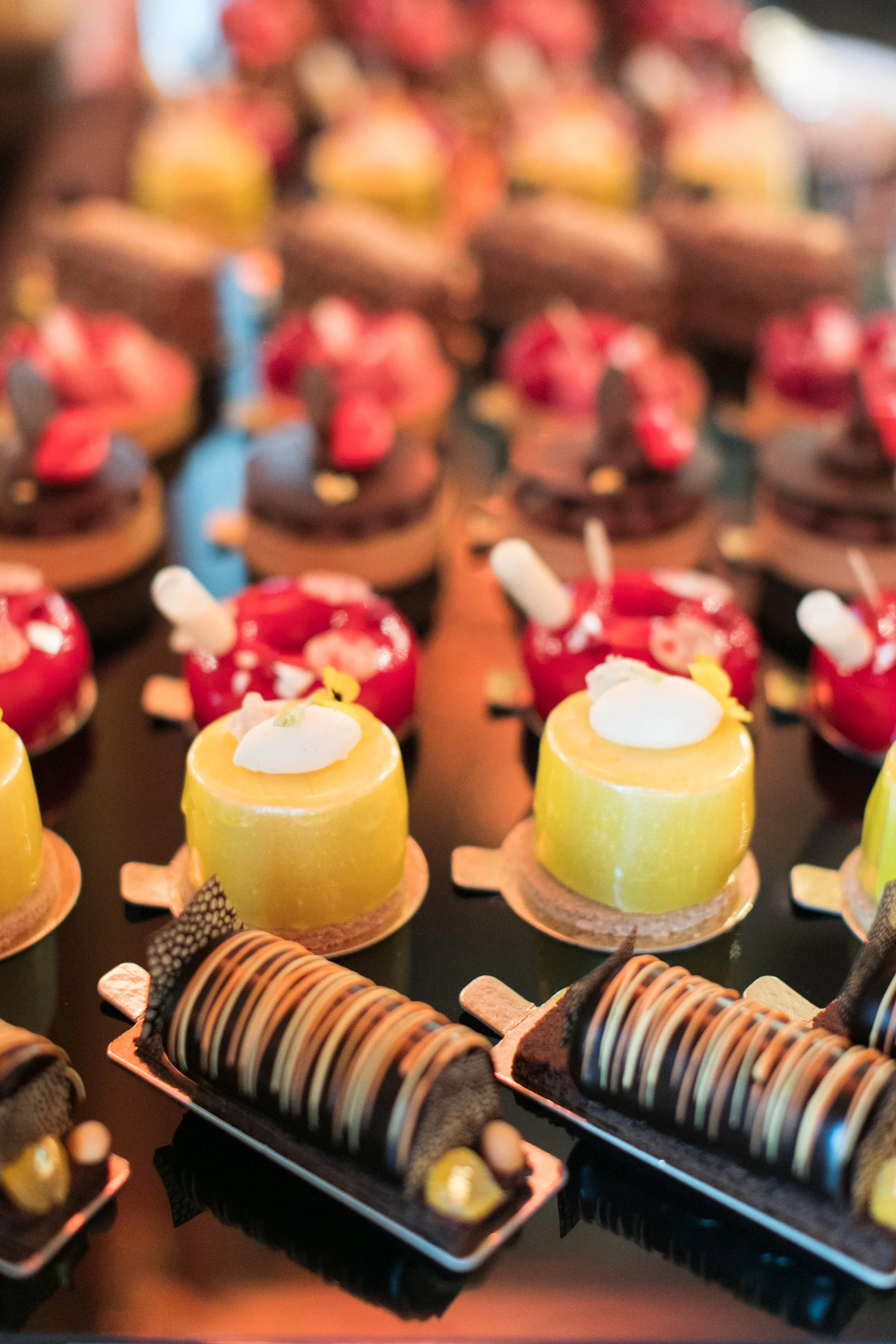 Assorted individual mini desserts with colorful toppings, displayed on black trays, including chocolate and fruit-flavored cakes and pastries.