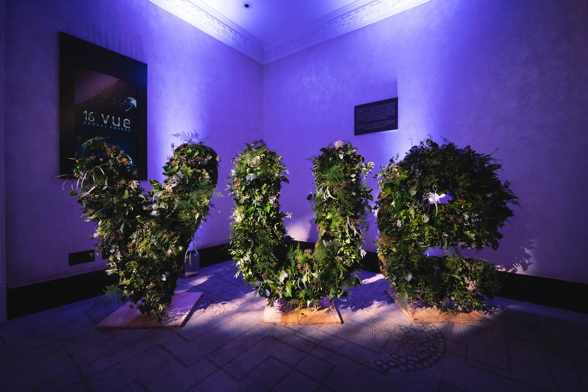 Flower arrangements on display at the 16th VUE Annual Awards event, illuminated by purple lighting in an indoor setting.