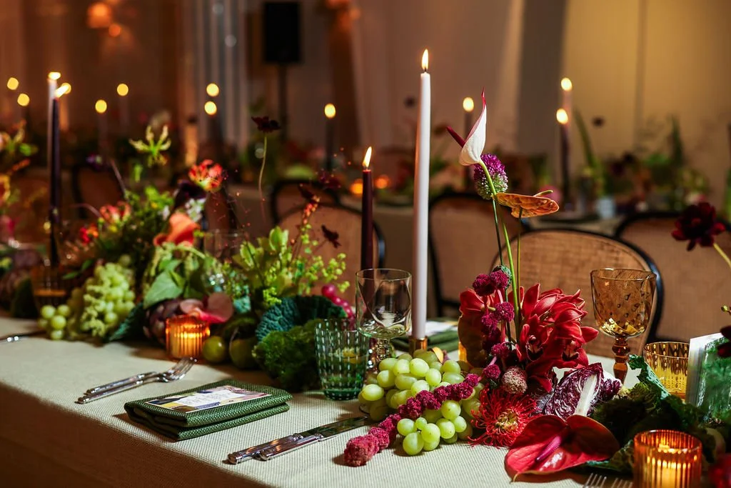 Elegant dining table decorated with candles, green grapes, and vibrant flowers, set for a wedding 