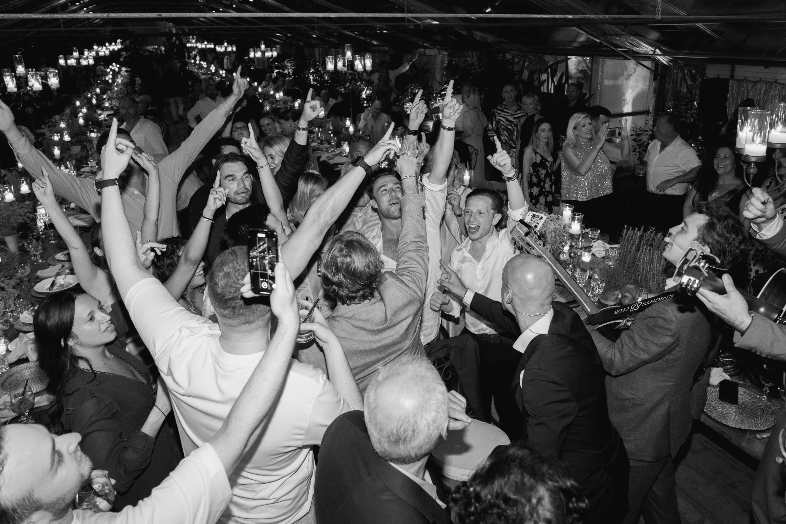 A lively indoor celebration with many people dancing and taking photos, illuminated by numerous candles and decorative lighting in Tuscany at Serre Torrigiani Bistrot
