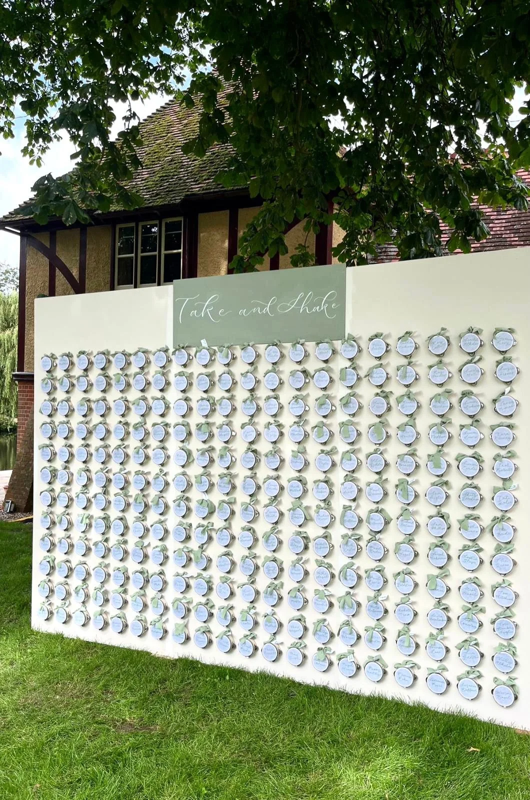 Decorative wedding display with small round cards attached to a white board, labeled 'Take and Shake'.