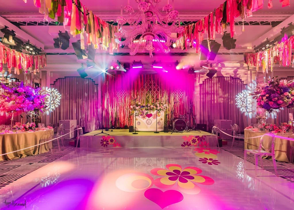 Claridge's decorated for a 70s themed Bat Mitzvah with pink lighting, flower arrangements, and hanging colorful ribbons for a party 