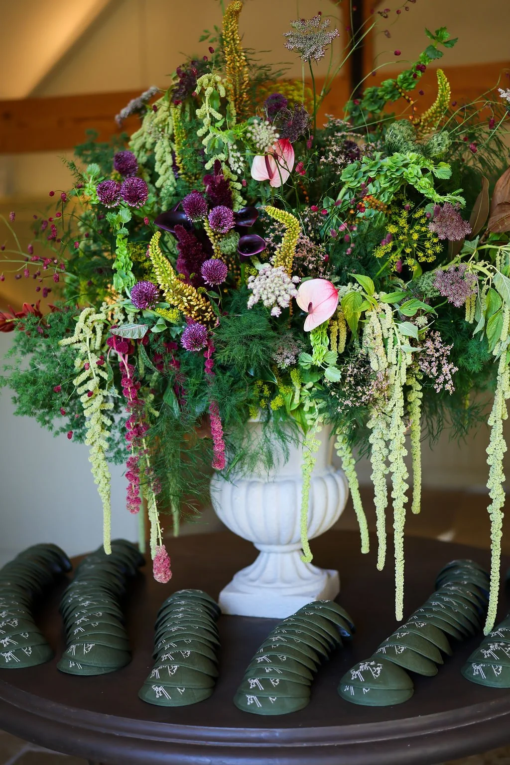 A large floral arrangement in a white vase featuring purple, pink, white, and green flowers and greenery, with kippah laid out in front of it on a dark surface.