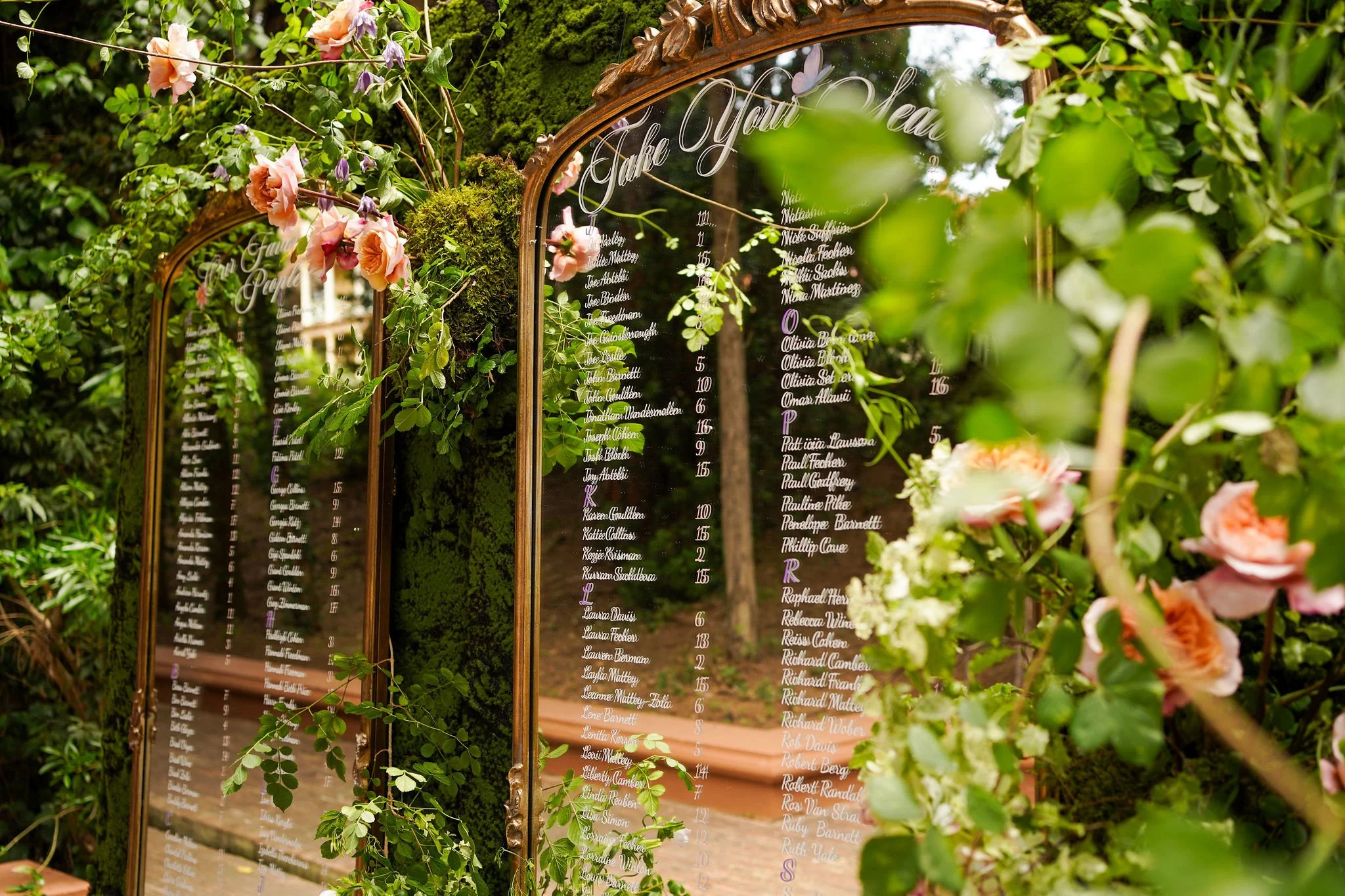 A decorative wedding seating chart mirror surrounded by greenery and pink flowers at Anantara Villa Padierna Resort in Marbella