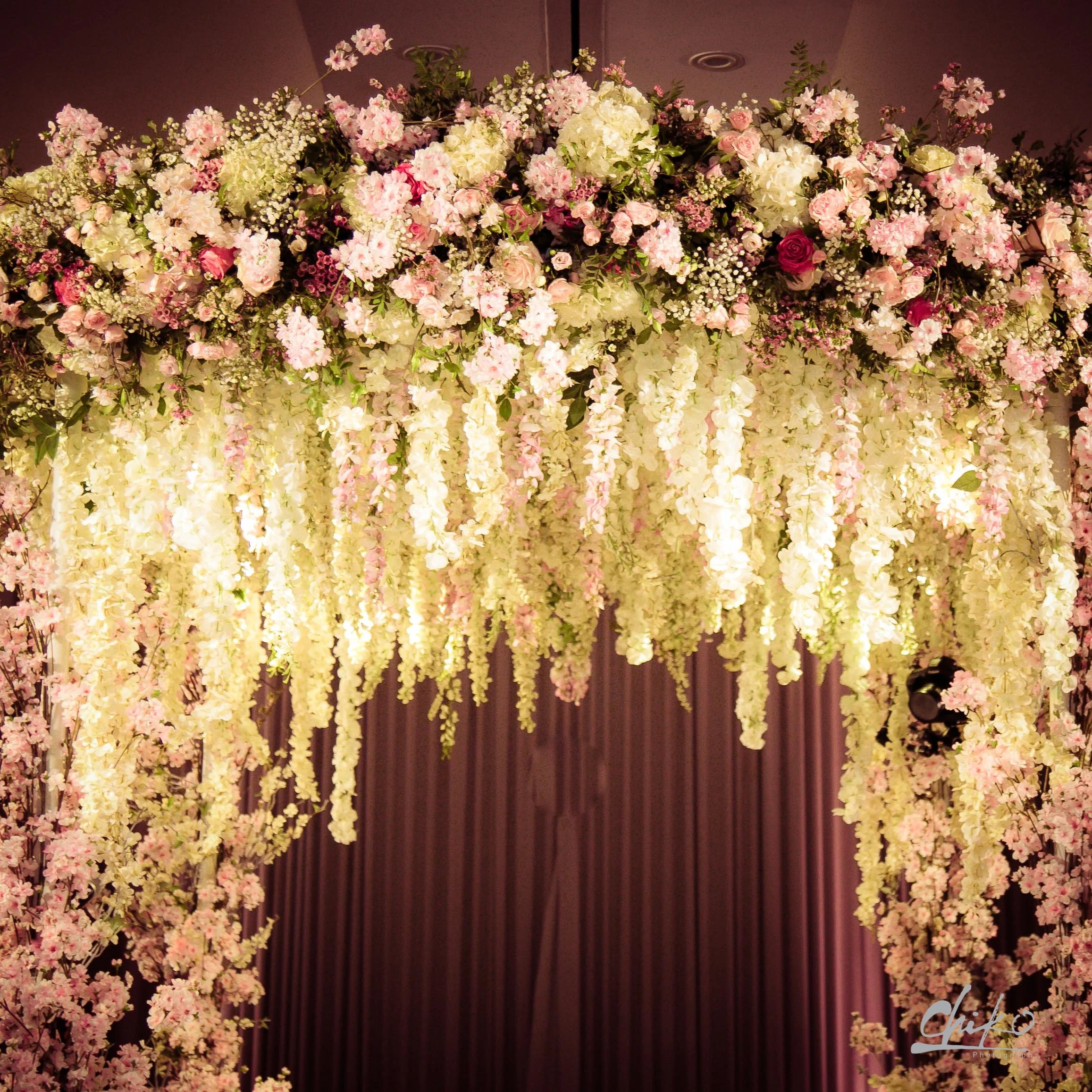 A large floral arrangement with pink, white, and cream flowers, hanging down from the ceiling with cream-colored curtains in the background at Rosewood London