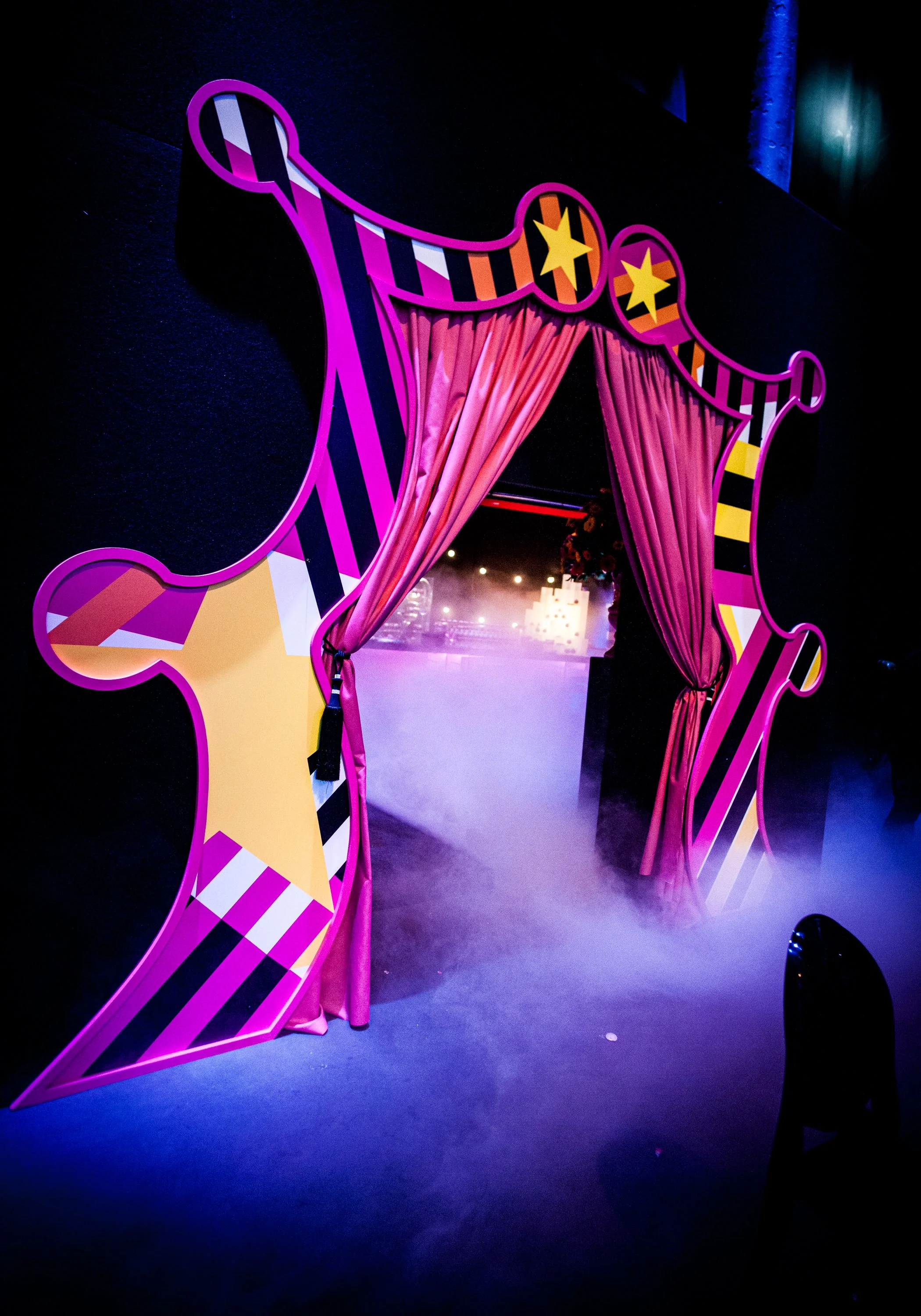 Decorative entrance arch with pink curtains and colorful striped and star patterns in a dark, dimly lit environment.  Bat Mizvah the roundhouse