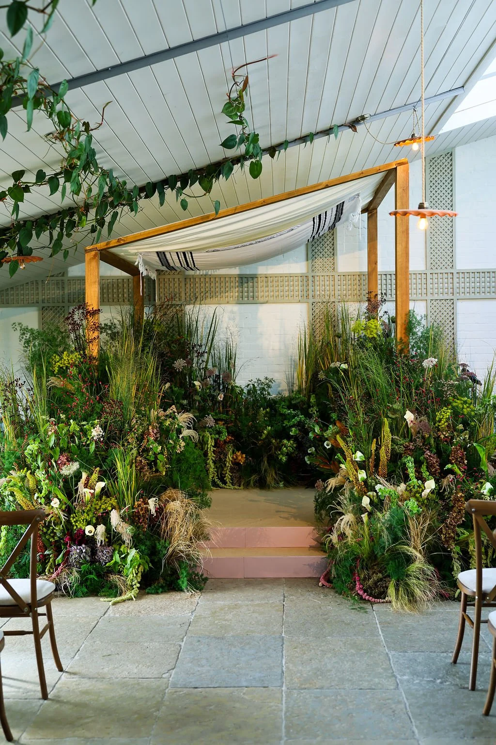 Kin House decorated with a floral Chuppah hanging lights, wooden canopy with a fabric drape, and chairs for seating.