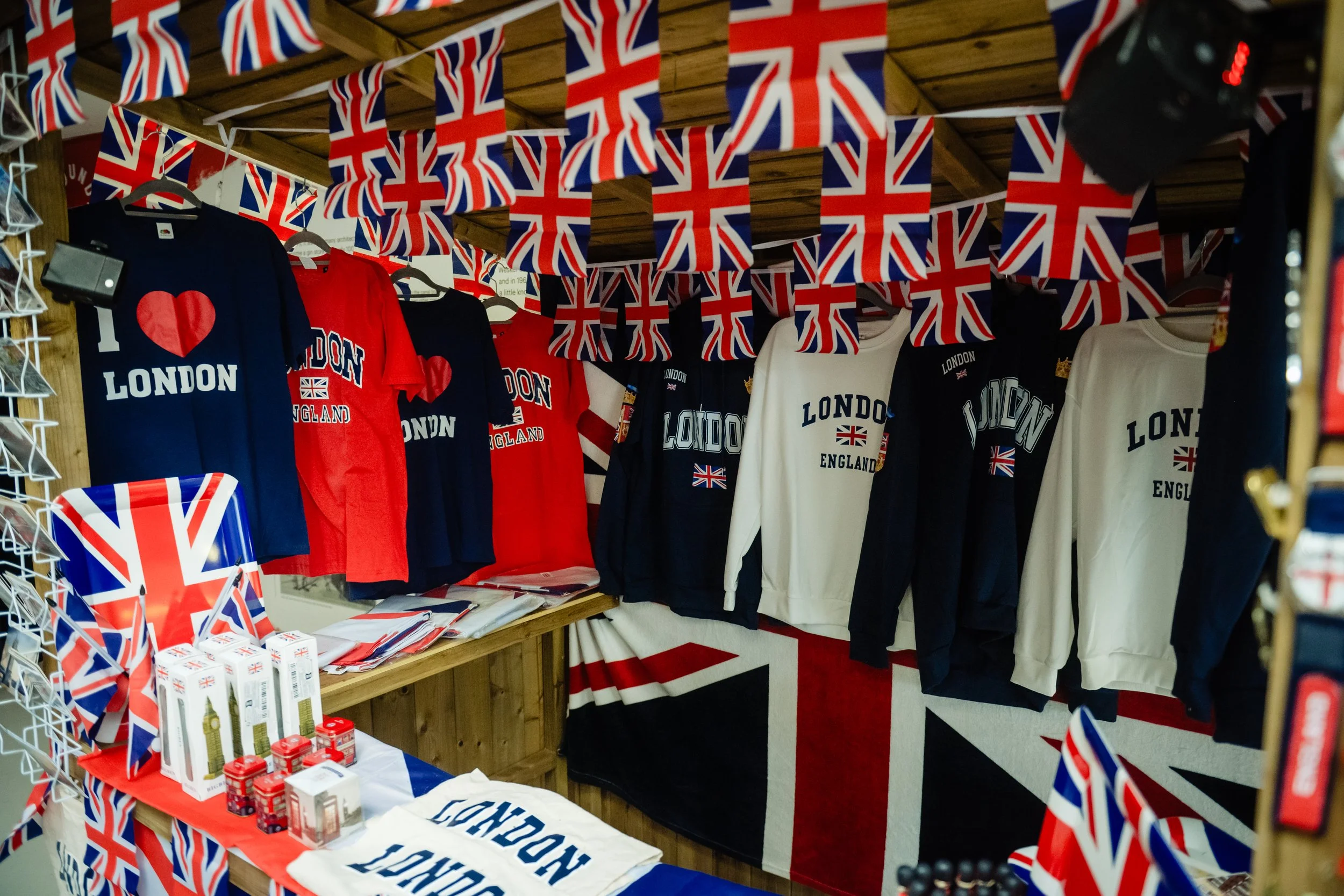A display of British-themed merchandise including Union Jack flags, T-shirts, and souvenirs on shelves and tables, with festive decorations.