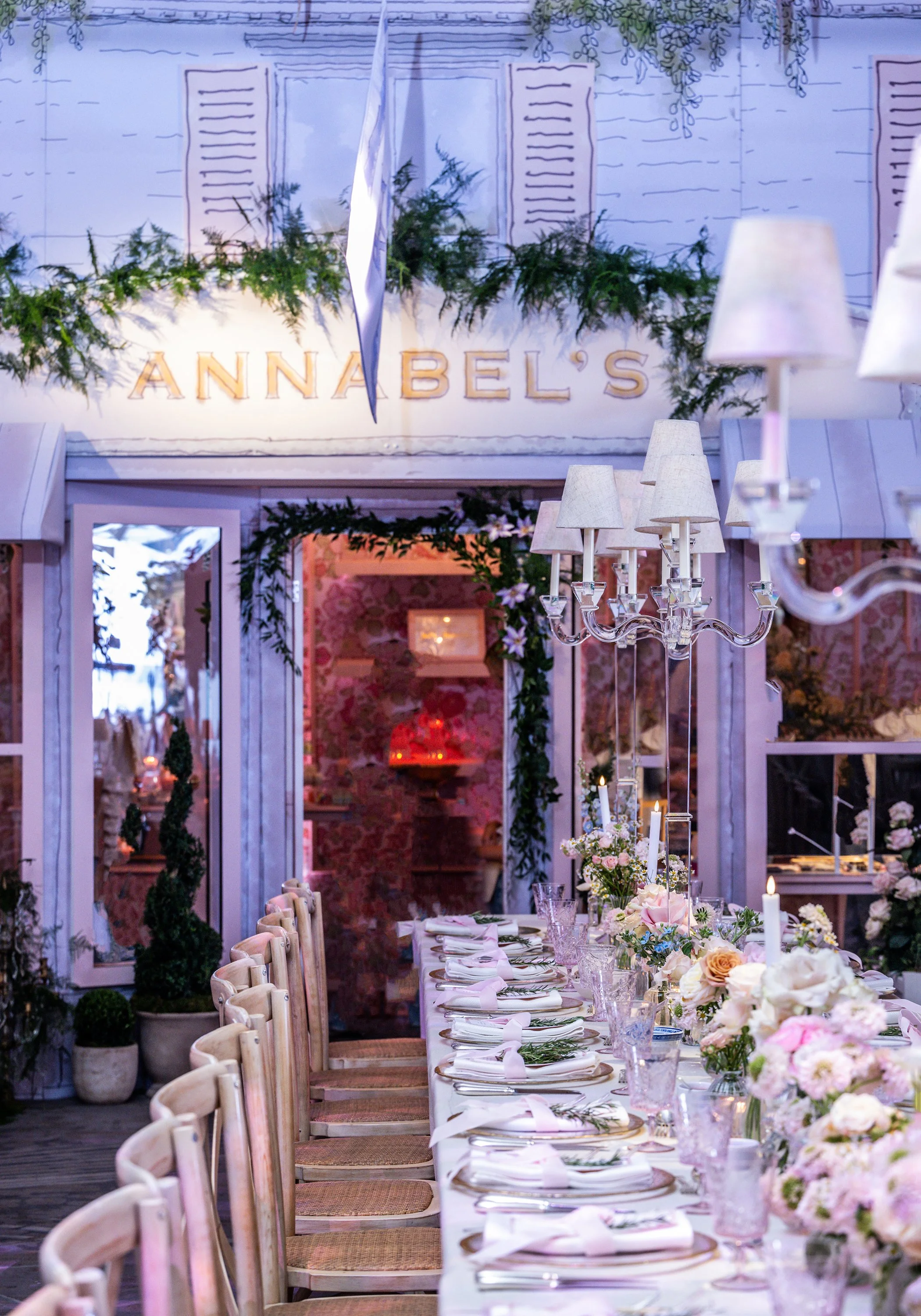 Elegant banquet table decorated with pink and white flowers, candles, and glassware, set up for a formal event with chairs along the sides, and decorated walls with greenery and floral arrangements in the background at Grosvenor House on Park Lane 