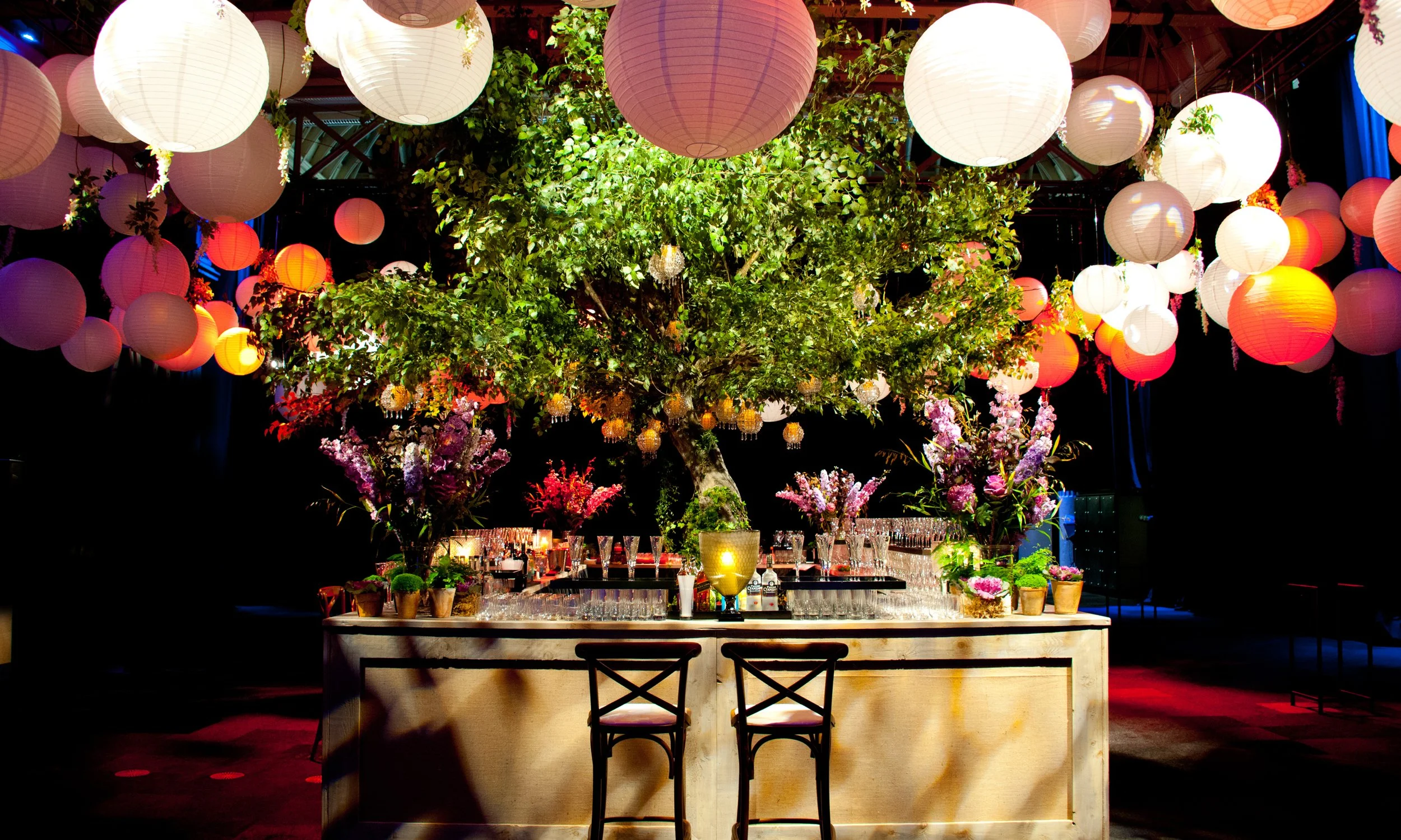 Decorative indoor setup with hanging paper lanterns, a large central tree, and floral arrangements on a table, creating an elegant and festive ambiance