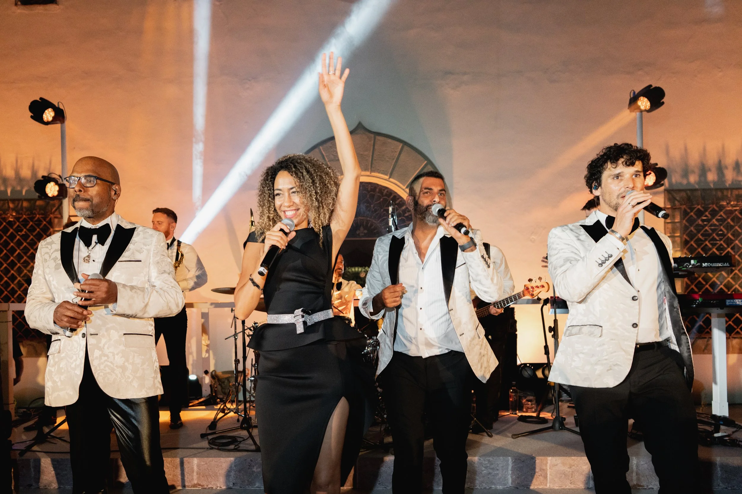 A group of musicians and singers performing on stage with microphones and musical instruments, under stage lights at Villa Palmieri in Florence