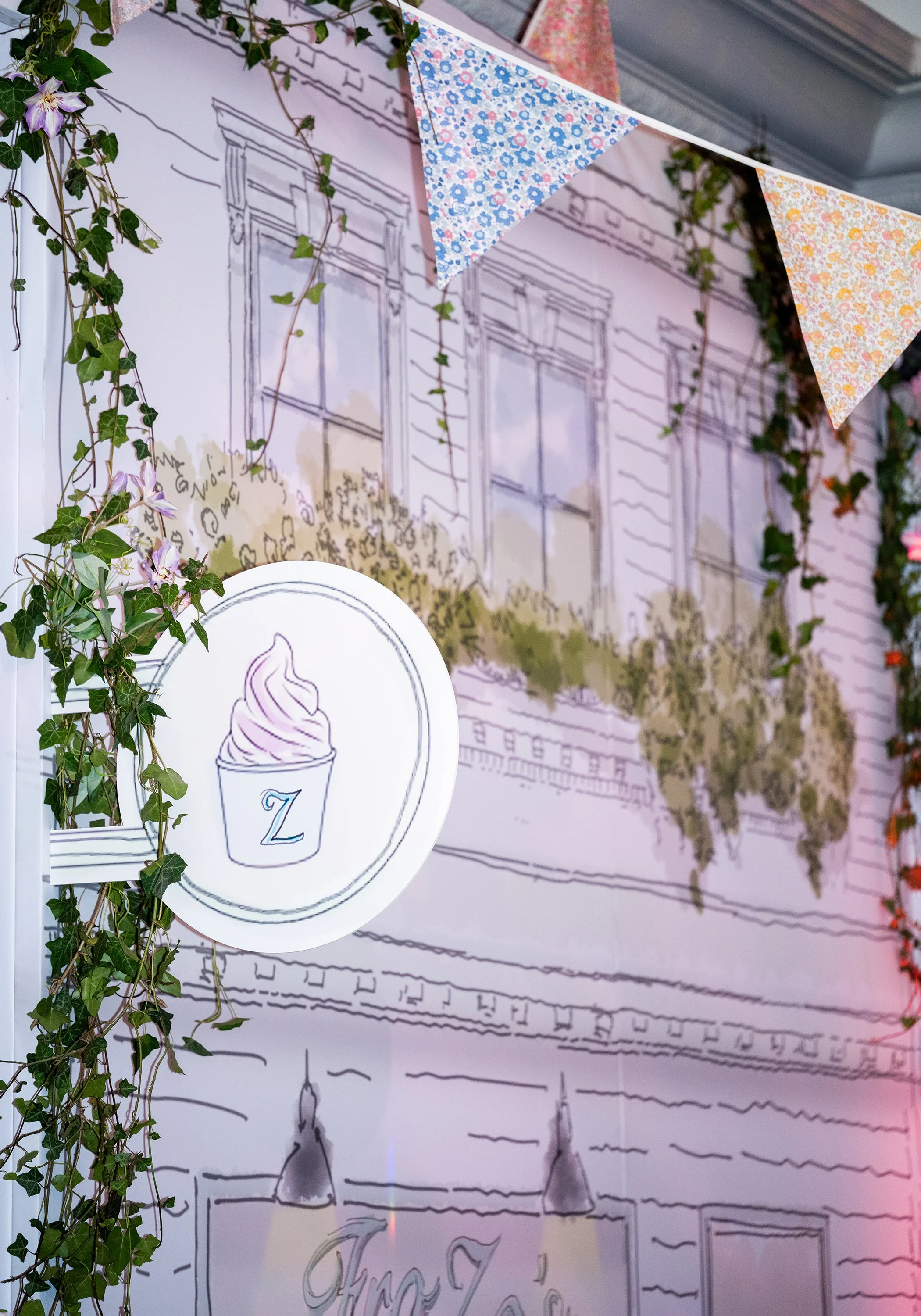 A wall with a sketch of a building facade, decorated with hanging fabric bunting flags with floral patterns, and greenery including ivy and other plants at Grosvenor House on Park Lane 
