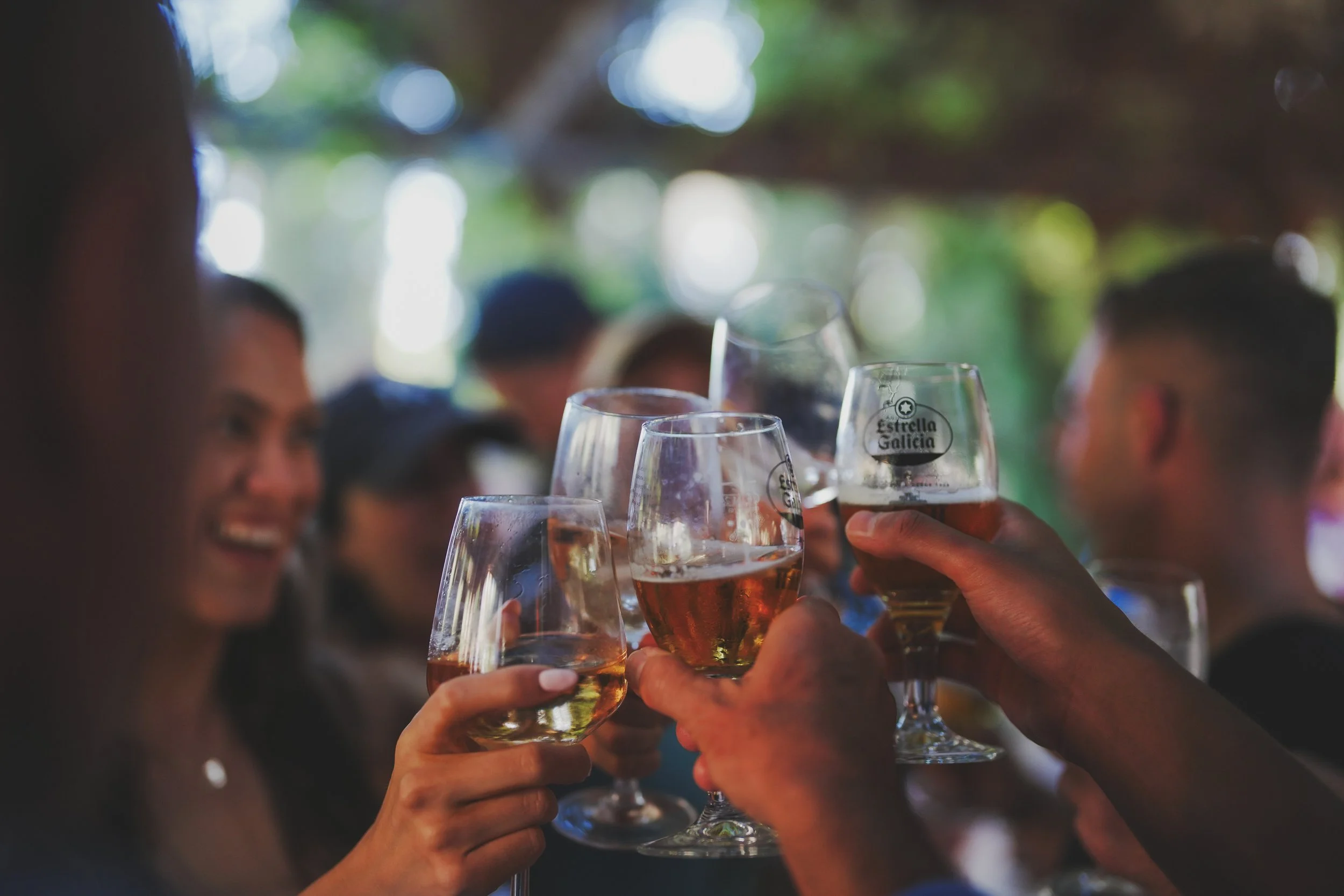 Group of people raising glasses of rosé wine in a toast at an outdoor gathering with blurred greenery in the background.