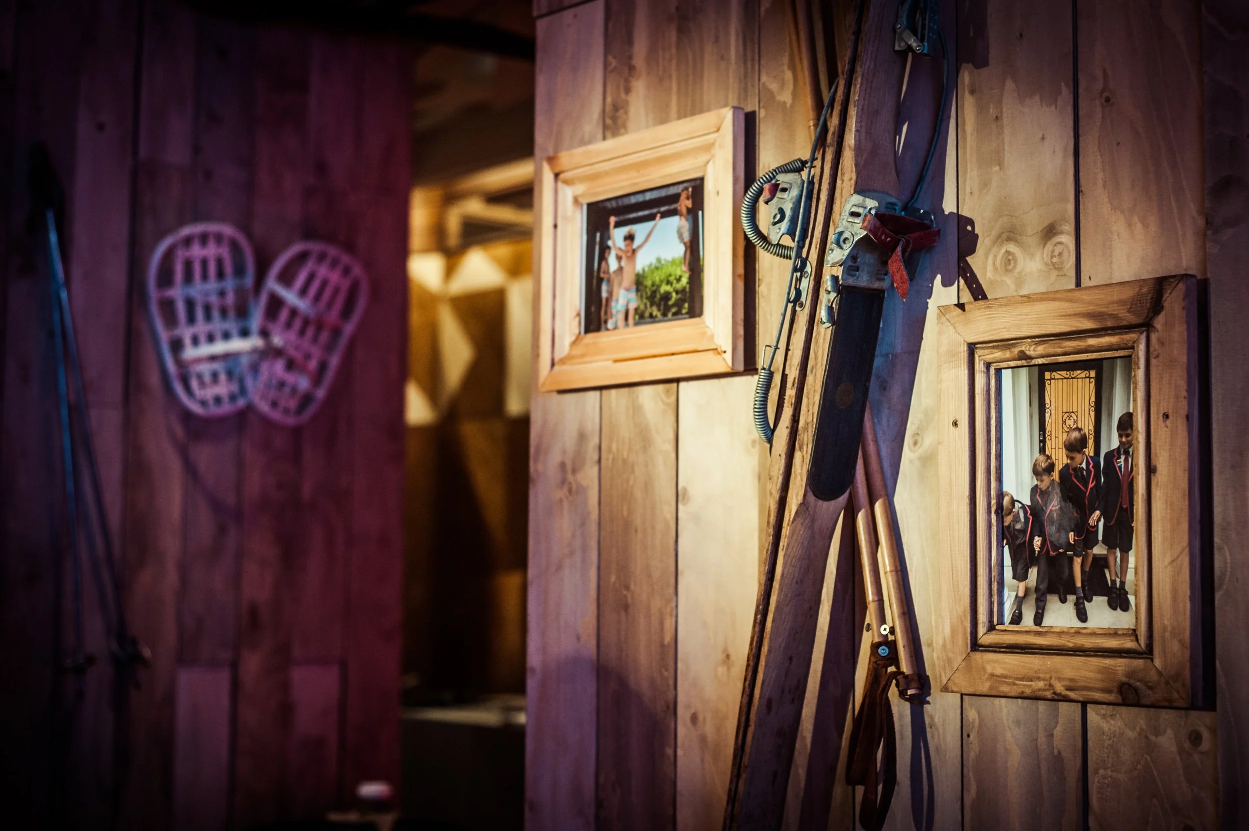 A wooden wall with framed photographs and attached tools, including a ladder, in a rustic indoor setting.