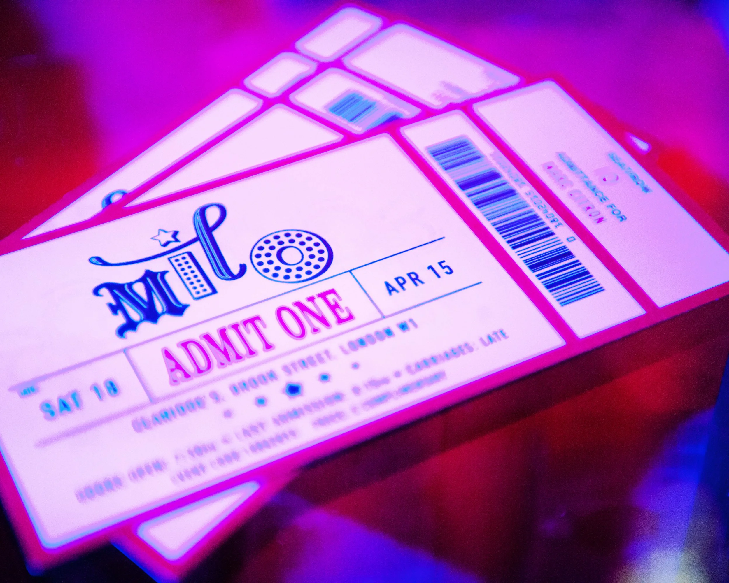Close-up of two pink lottery scratch-off tickets under pink and blue neon lights, with the tickets partially reveal and a barcode visible.
