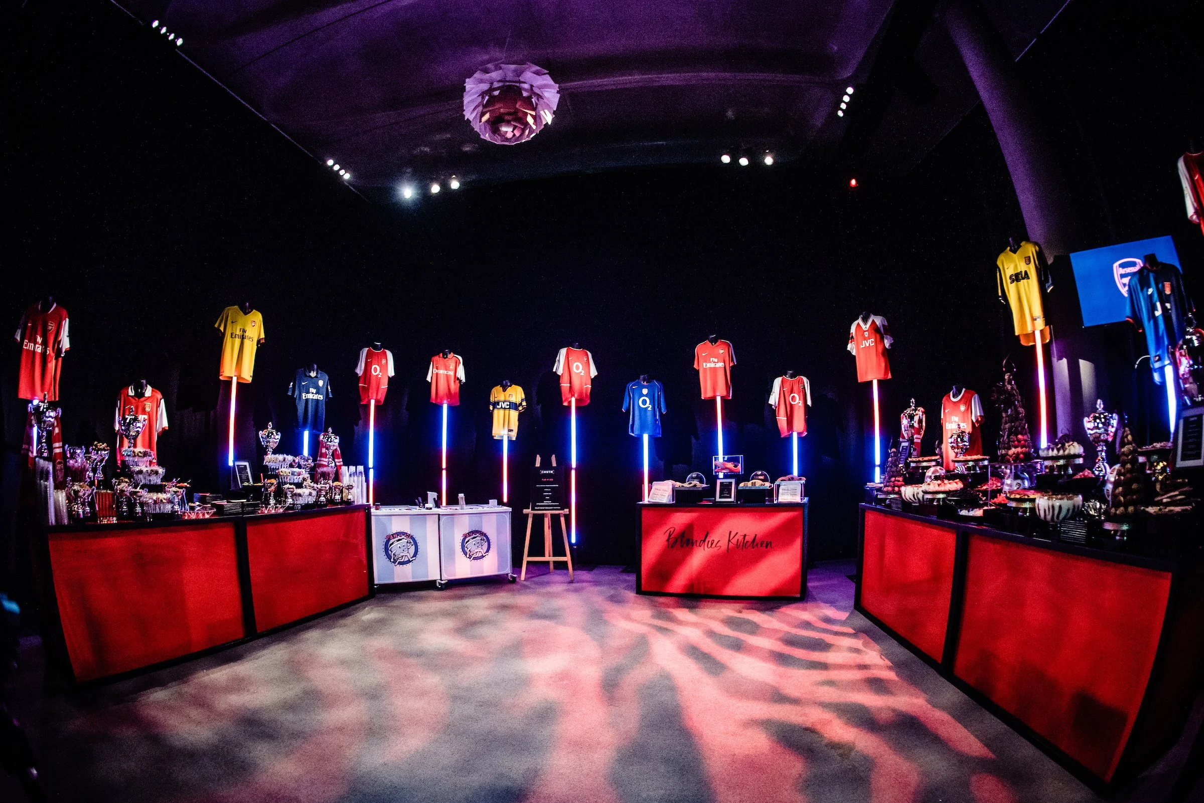 A display of sports jerseys hanging on illuminated poles inside a dark exhibition space.