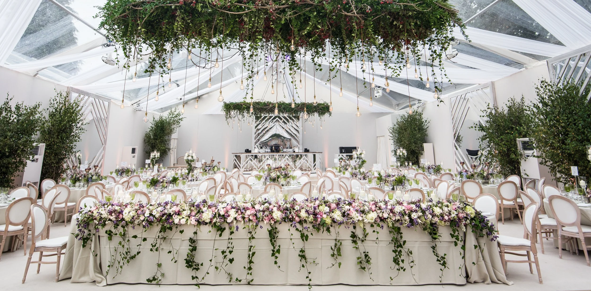 Elegant event venue decorated with floral arrangements and hanging greenery, with tables set for a celebration.