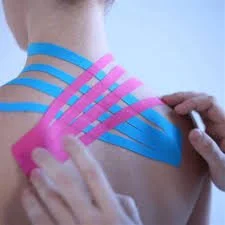 Person applying pink kinesiology tape to shoulder with blue tape nearby.