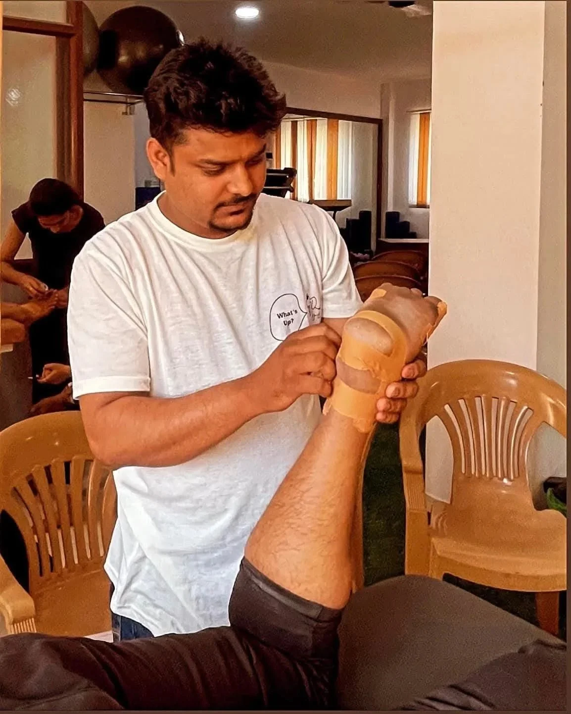 A man receiving leg massage from a therapist in a room with chairs and windows.