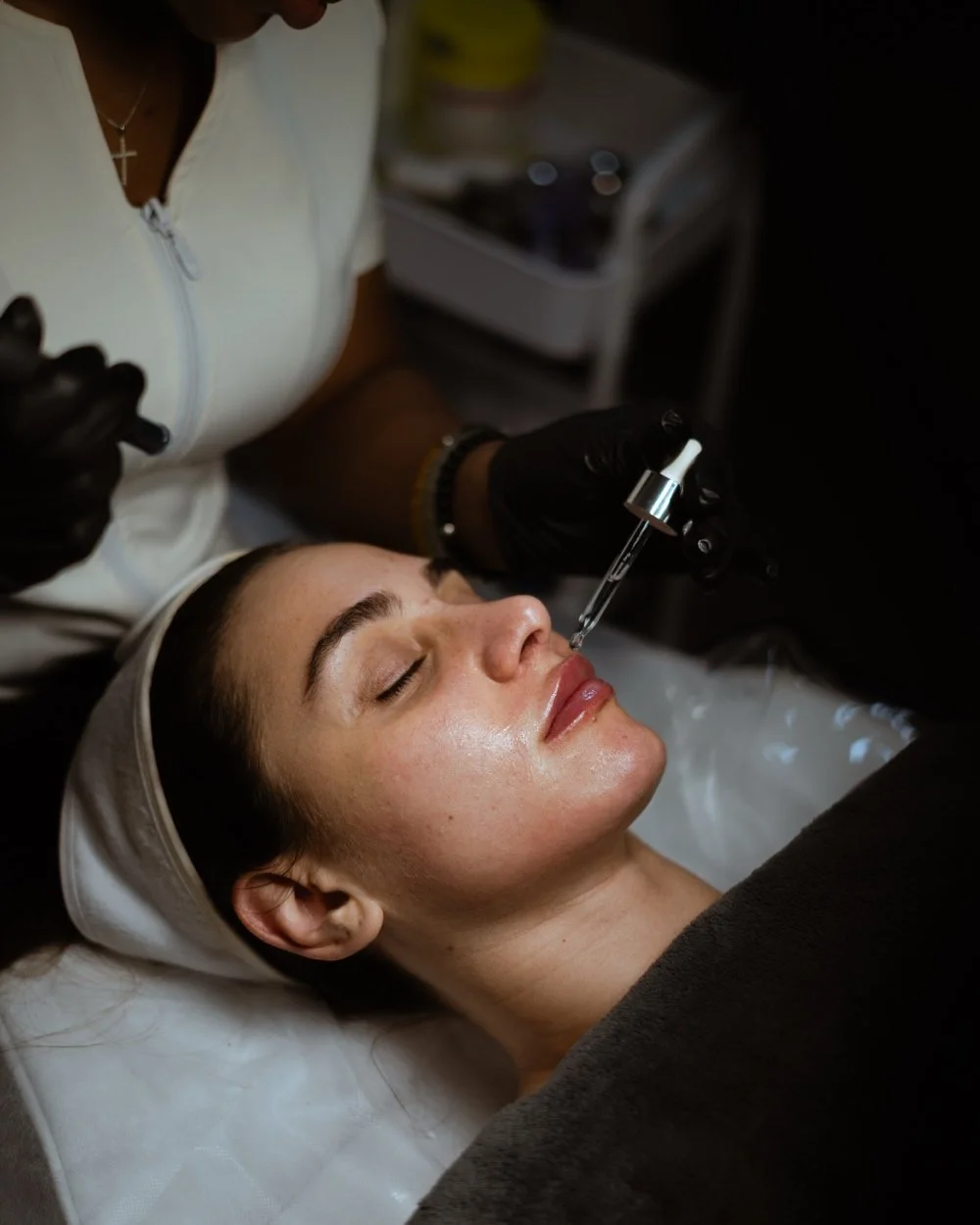 A woman receiving a cosmetic facial injection from a professional wearing black gloves in a clinic.