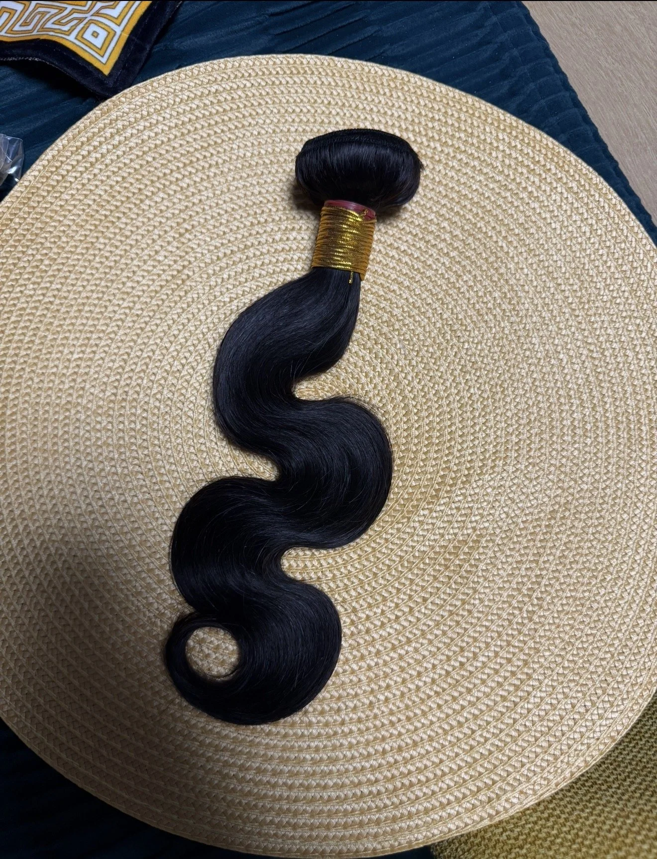 A bundle of wavy black hair secured with a gold band, placed on a woven circular mat.