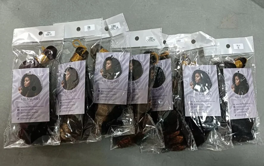 Multiple small plastic bags containing hair extensions, with business cards from Milbacashi Hair, featuring images of women with styled hair.
